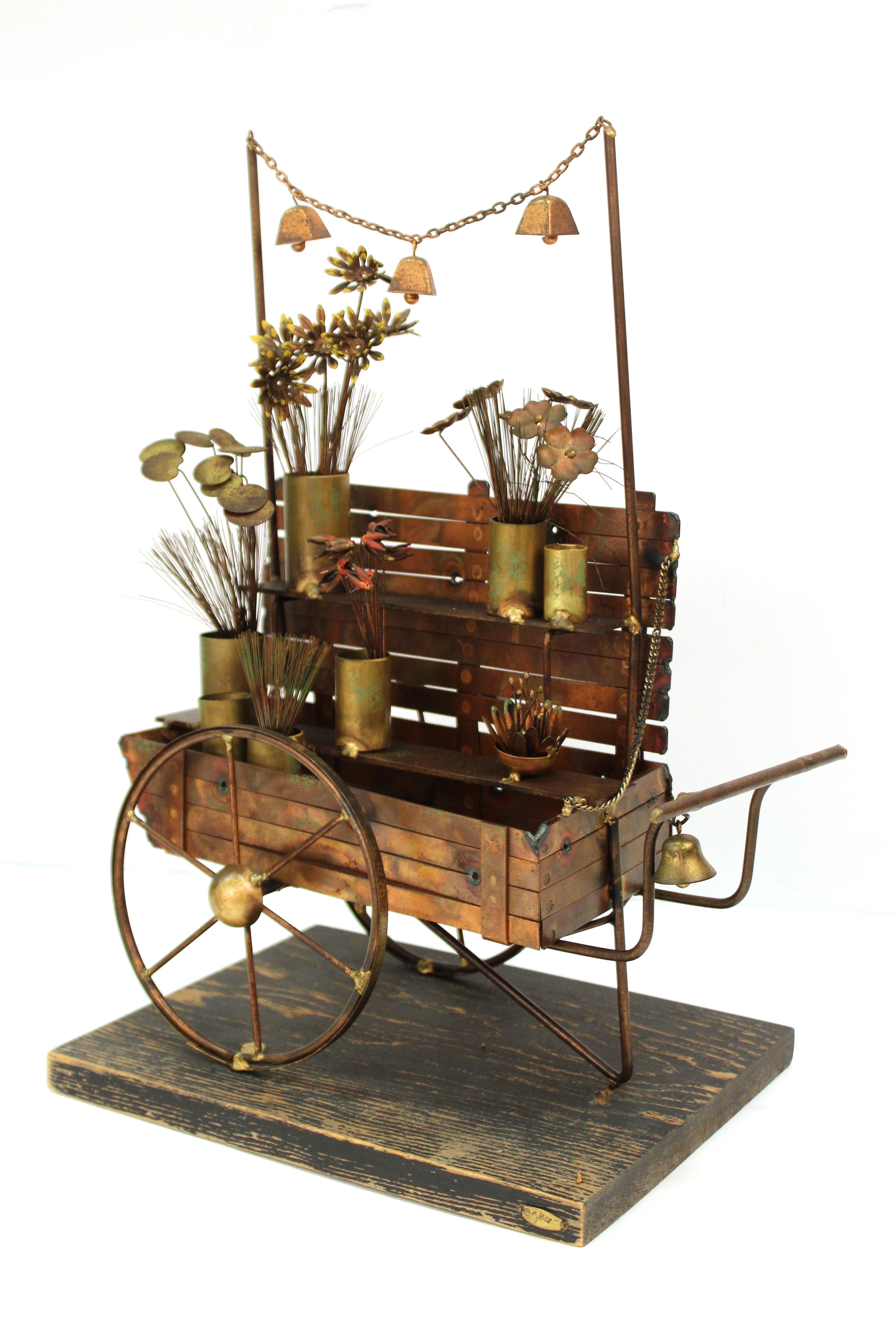 A Mid-Century Modern flower cart sculpture made by Curtis Jere in copper and brass on a wooden platform during the 1960s-1970s. Intricate detailing with flowers and baskets, with a little functioning bell hanging on the cart. Wear to metal but