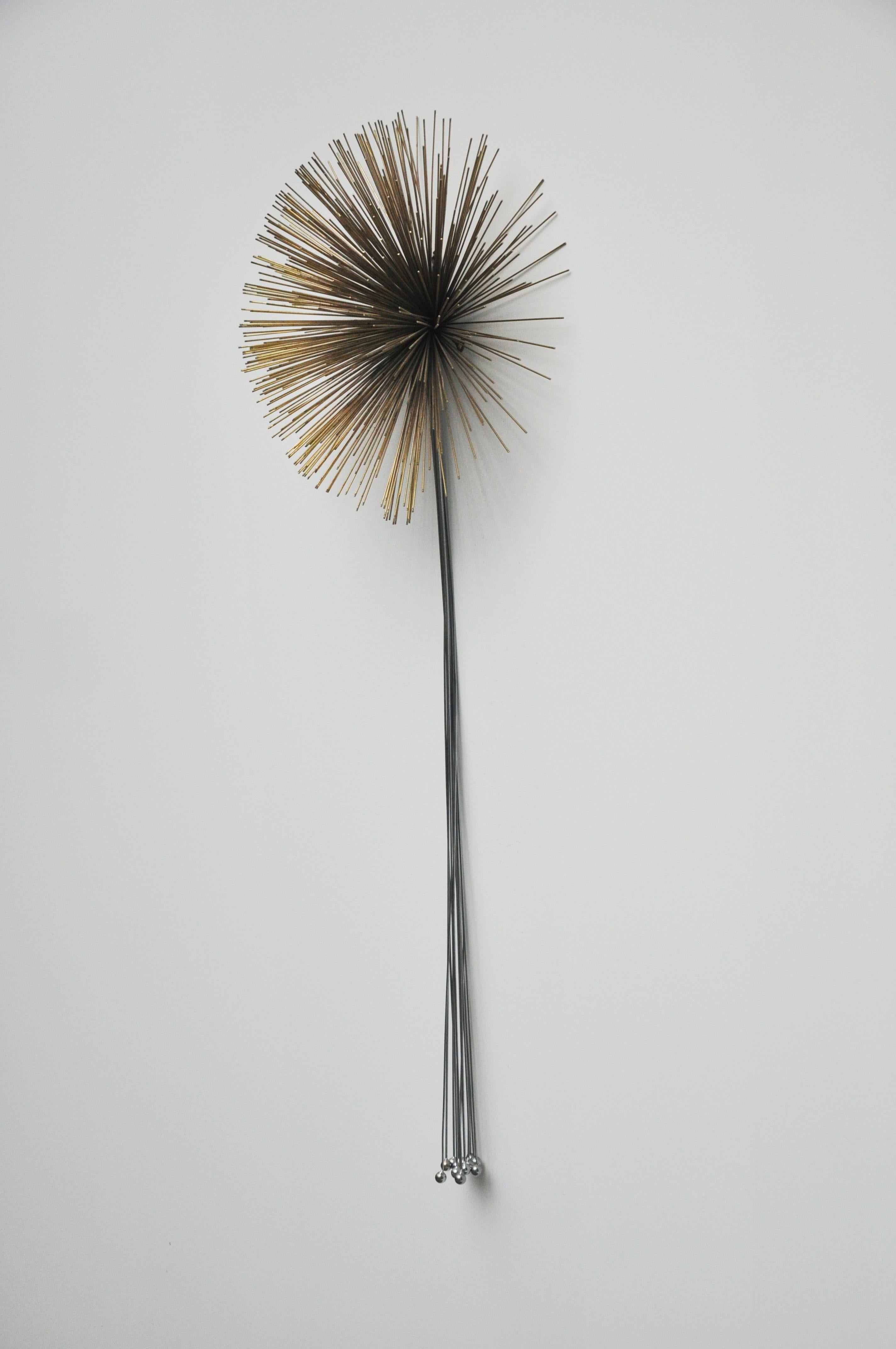 This wall sculpture was designed by Curtis Jere. The piece is a Mid-Century Modern and is created from mixed metals. It is created from thin metal rods welded together to make a dimensional starburst. The sculpture is signed and dated 1988.