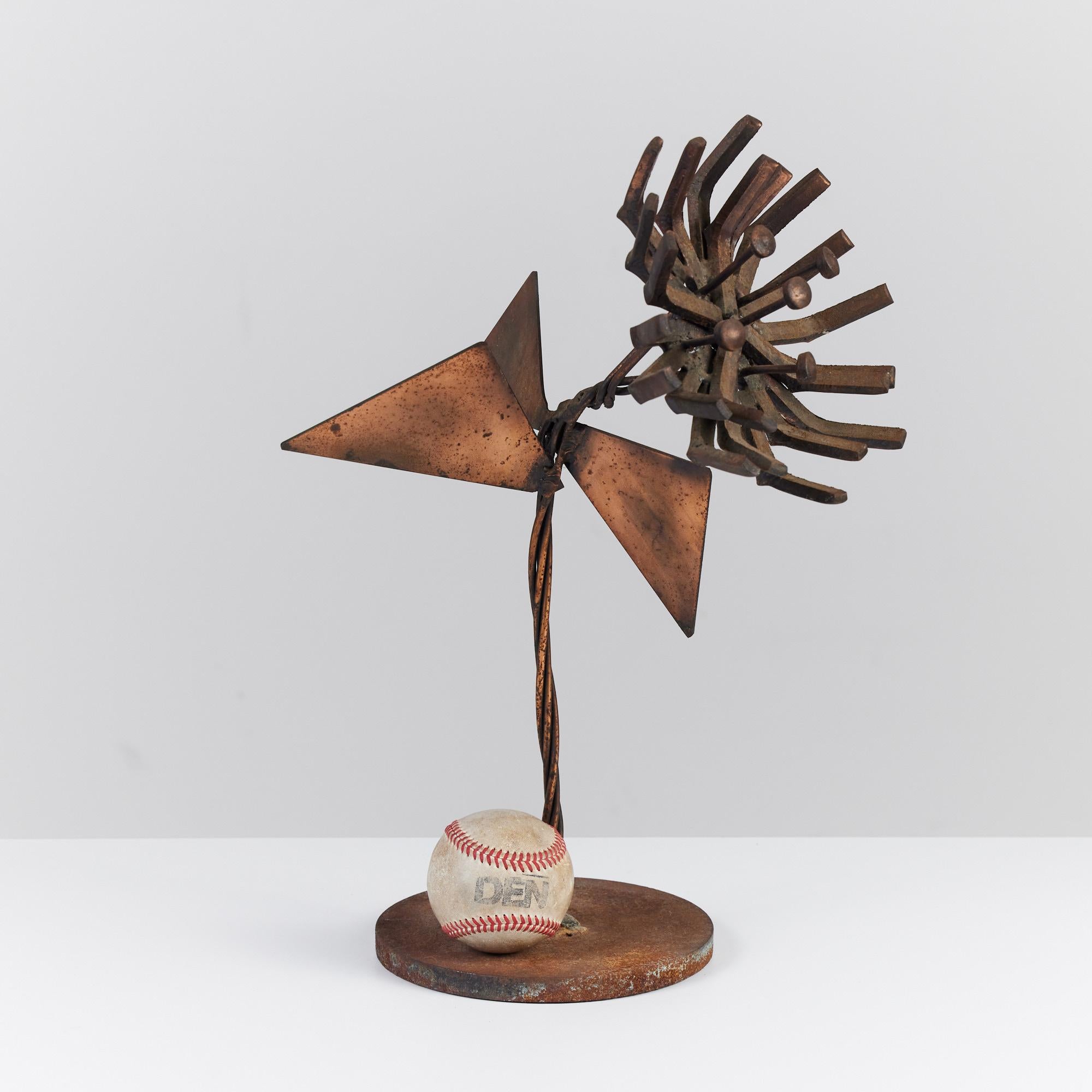 A brutalist mid century flower sculpture in the style of Curtis Jeré. The mounted sculpture features a twisted stem that branches out to three triangular leaves. The flower features bent metal petals offering a sunburst shape. The patina is