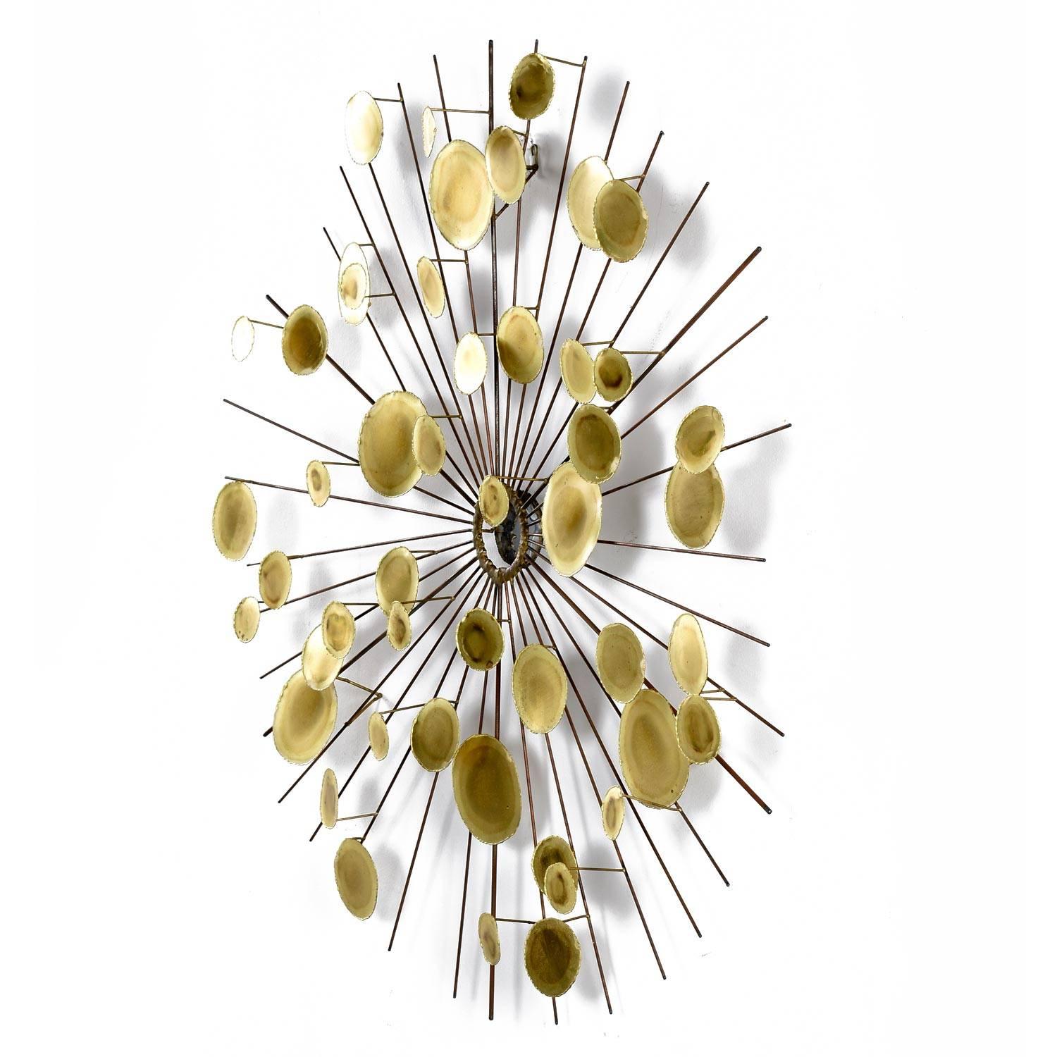 This striking Mid-Century Modern large sunburst wall sculpture is in the style of Curtis Jere, circa 1970s. Metal spires radiate from the mirrored brass centre and expand outward with three-dimensional gold tone polished brass medallions welded into