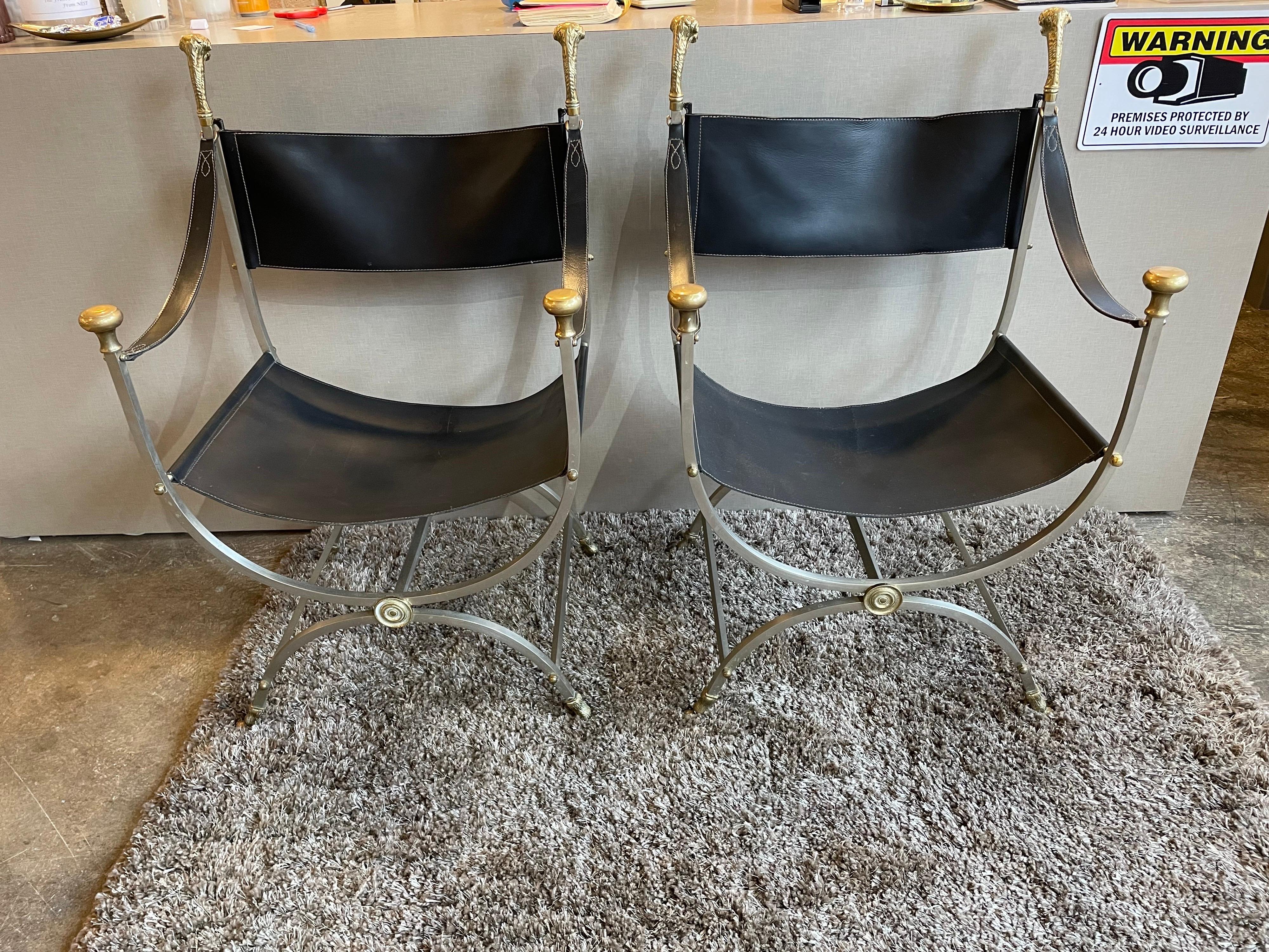 This is a wonderful pair of steel, and black leather chairs with brass rams heads at top and brass hoof feet on legs These chairs are in the style of Maison Jansen and would make a lovely addition to someones home.