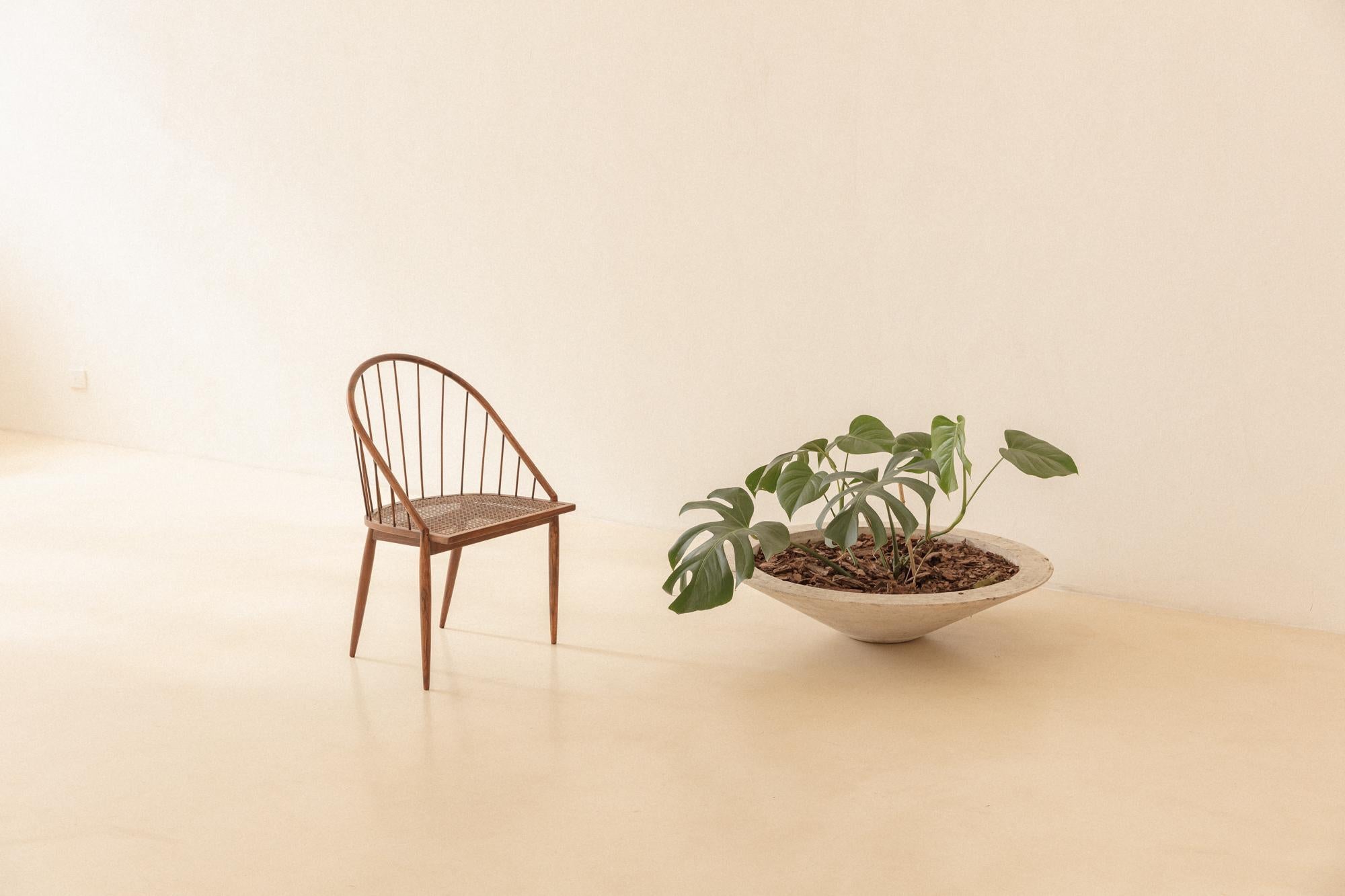 Cette chaise incurvée en bois de rose avec dossier en bâton, conçue par Joaquim Tenreiro (1906-1992) en 1961/1962, évoque la coexistence raffinée de valeurs traditionnelles et d'une esthétique moderne. Ses formes délicates, avec des dos de bâtons