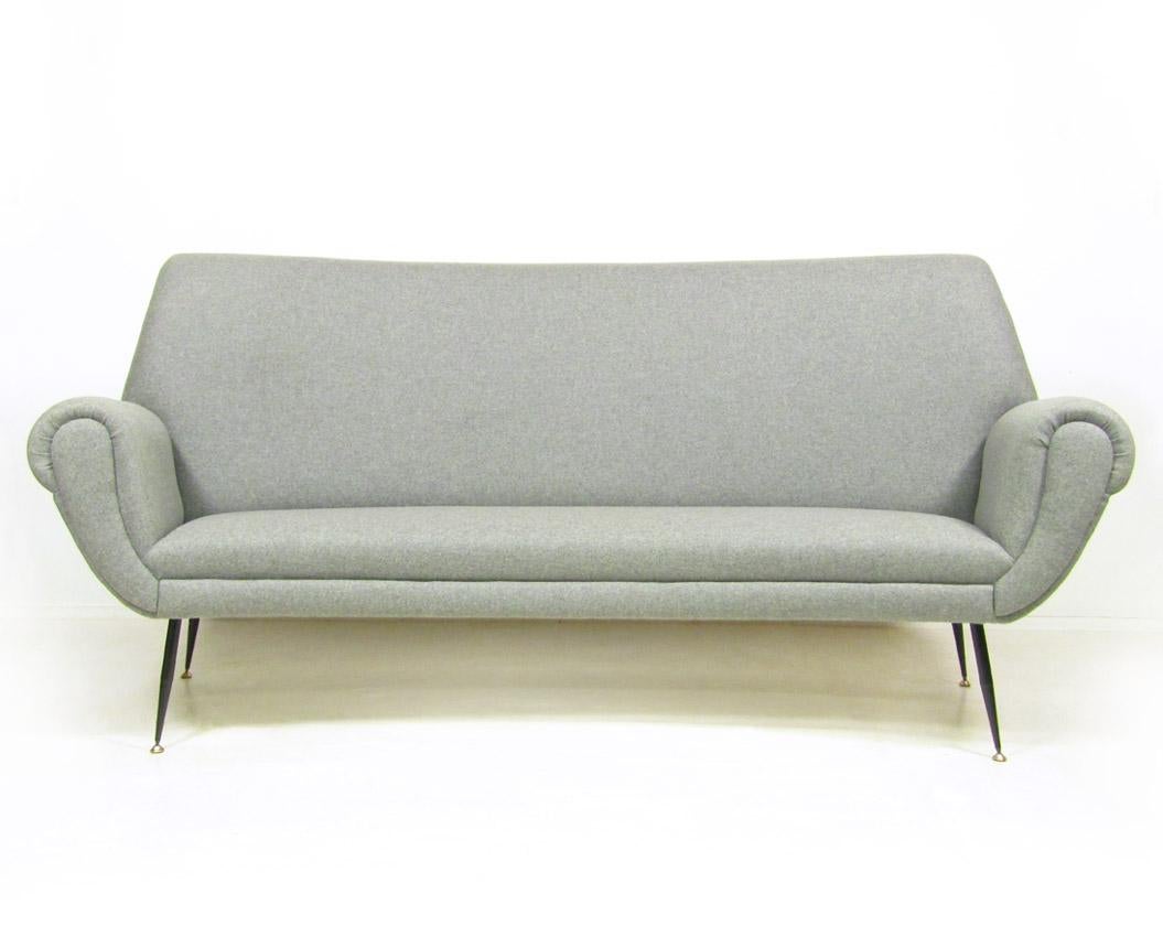 A gracefully curved 1960s Italian sofa by Gigi Radice.
 
It has been newly reupholstered in soft Italian mid-grey wool fabric. 

It rests on tapering, brass-tipped feet.
 
This three-seat sofa is extremely comfortable.
 
In excellent,