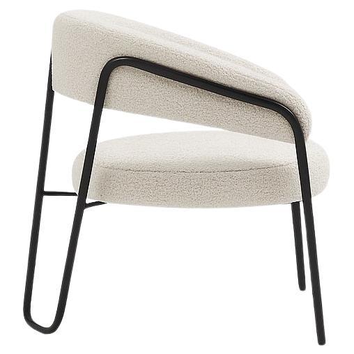 Este sillón tiene una silueta escultural con una fuerte presencia gráfica. Es una pieza moderna que mezcla una elegante estructura de metal oscuro con un asiento y un respaldo tapizados de felpa. Los reposabrazos y el respaldo forman una línea