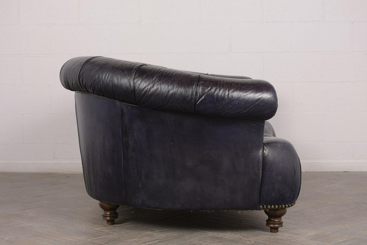 This 1970s Chesterfield-style sofa is upholstered in leather that has been dyed in a washed navy blue with an amazing distressed finish. The sofa features a curved seat back with a scroll edge. The front of the sofa features an inverted curve and