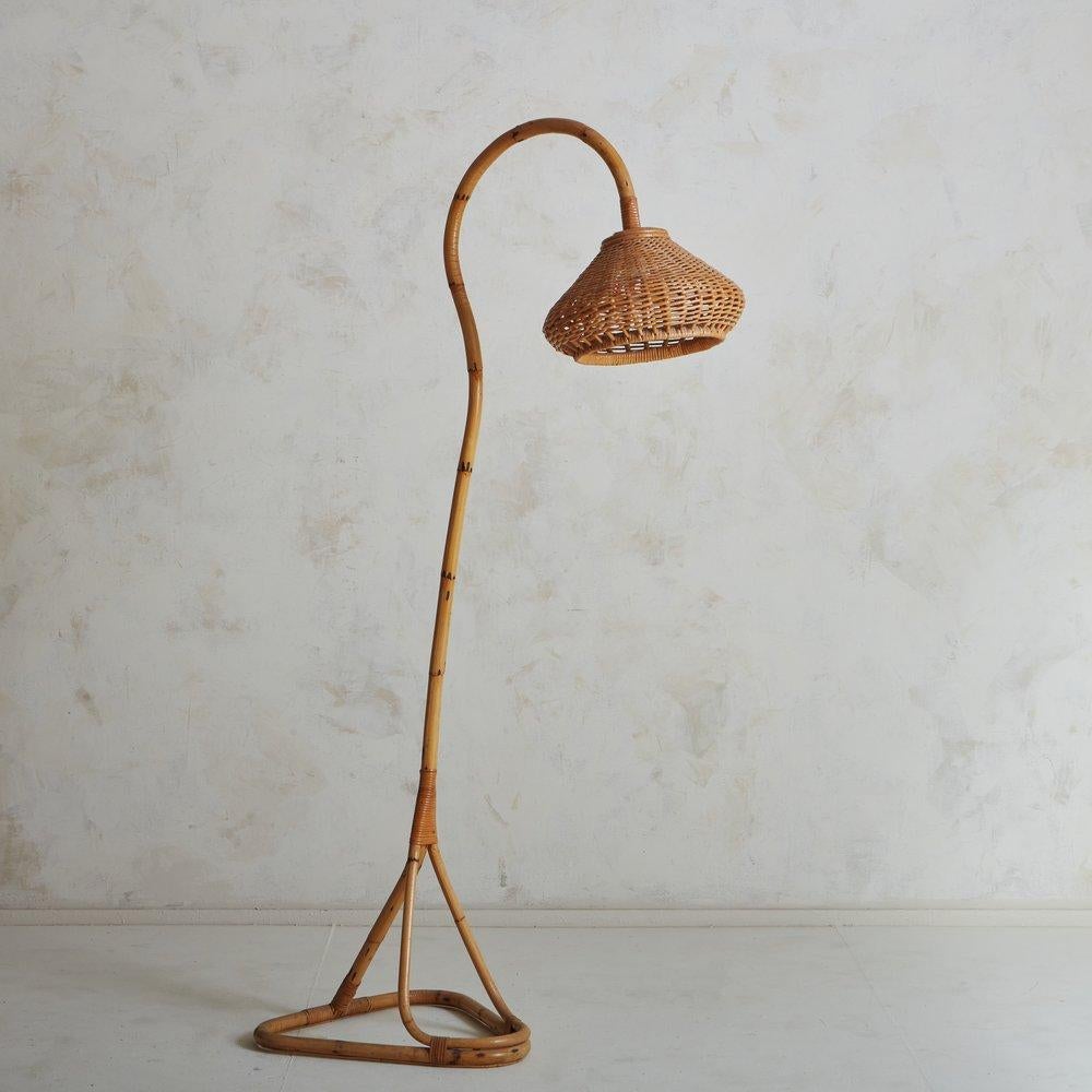 A sculptural vintage French floor lamp featuring a curved bamboo body and triangular tripod base. This unique lamp has beautiful cane detailing and retains its original wicker shade. Sourced in France, 1970s.

