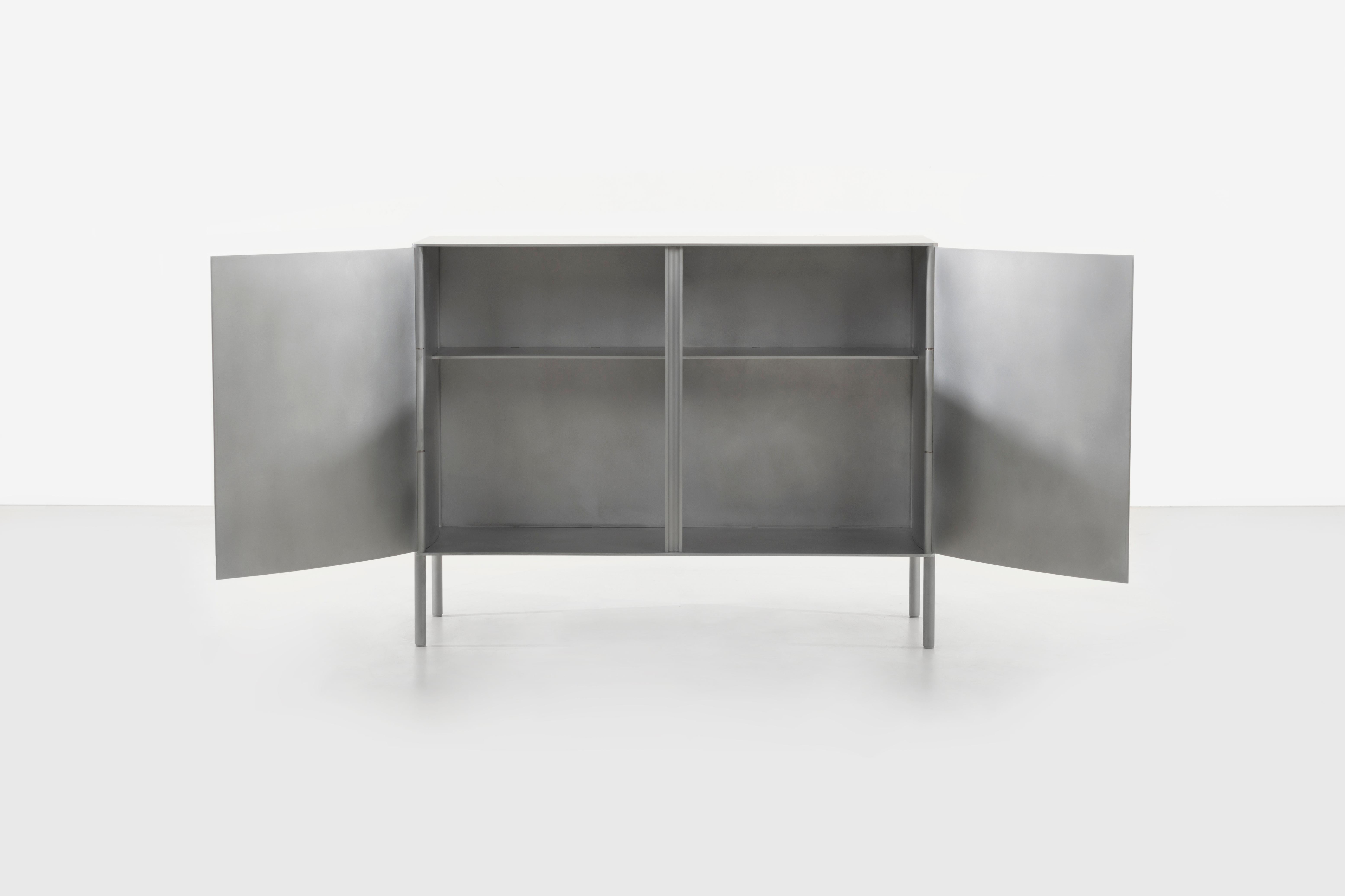 The curved cabinet by Jonathan Nesci is cut, rolled, and machined aluminum with a waxed finish. The doors, back and sides have a slight curve. The doors are cut and are welded to machined custom hinges and lap the center vertical piece slightly to