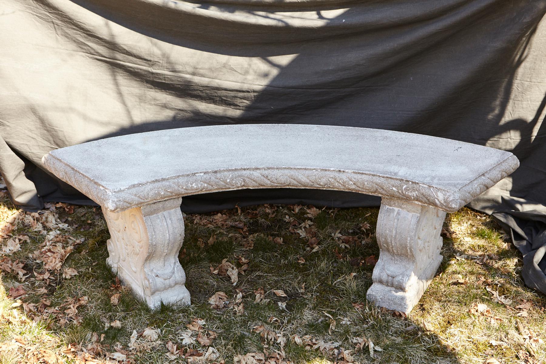 Curved cast stone bench with an ornamental carved band of alternating concave and convex sections around the flat seat, reminiscent of waves, mounted on carved legs with carved double-sided scrolled ornaments and leaves.
The bench has a very nice