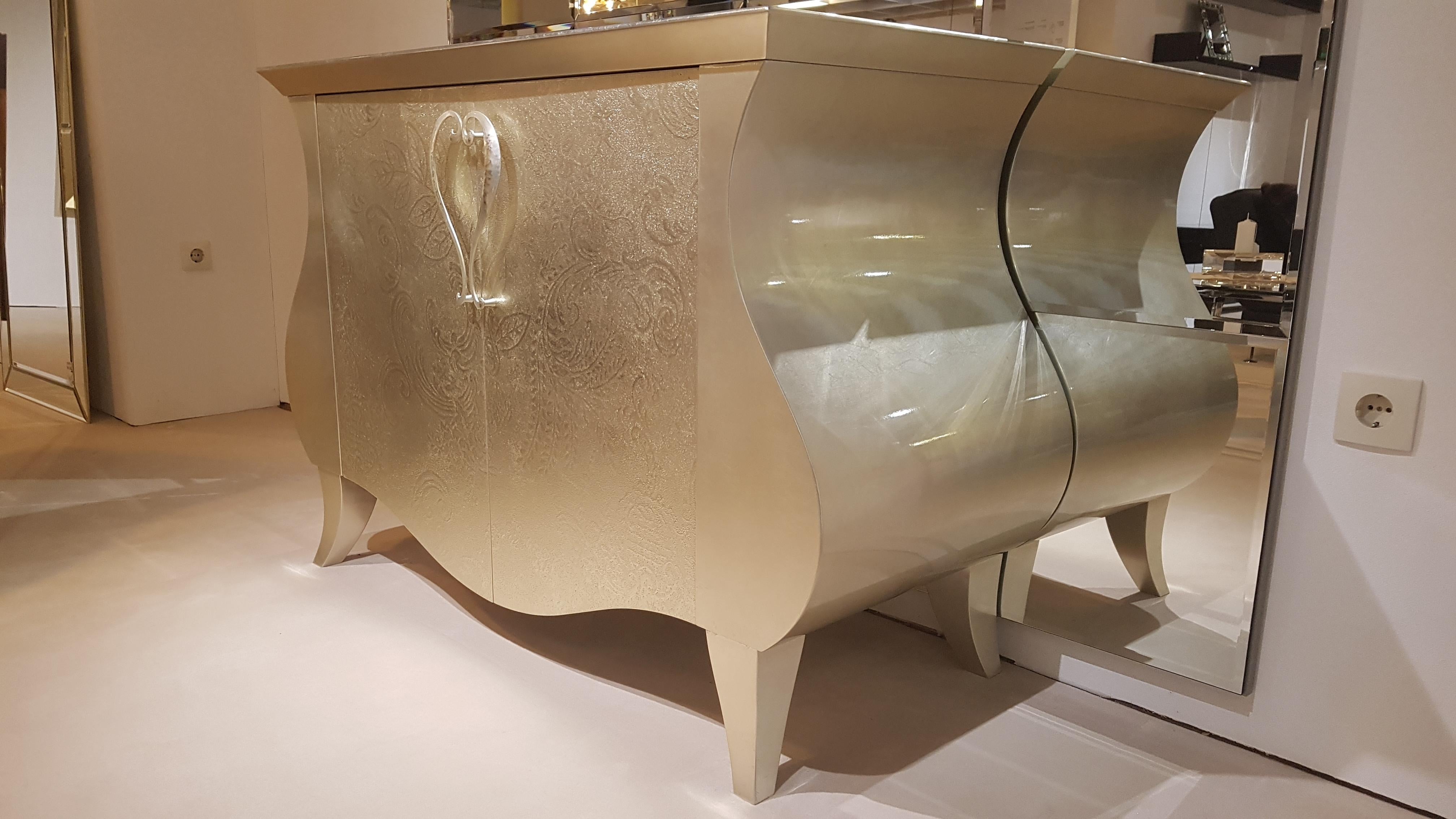Stunning curved commode with a beautiful design and a luxurious all around gold leaf finish with elegant floral ornamentations. The gold leaf convinces with its wonderful color and the high gloss finish. The complete body is curved like on original