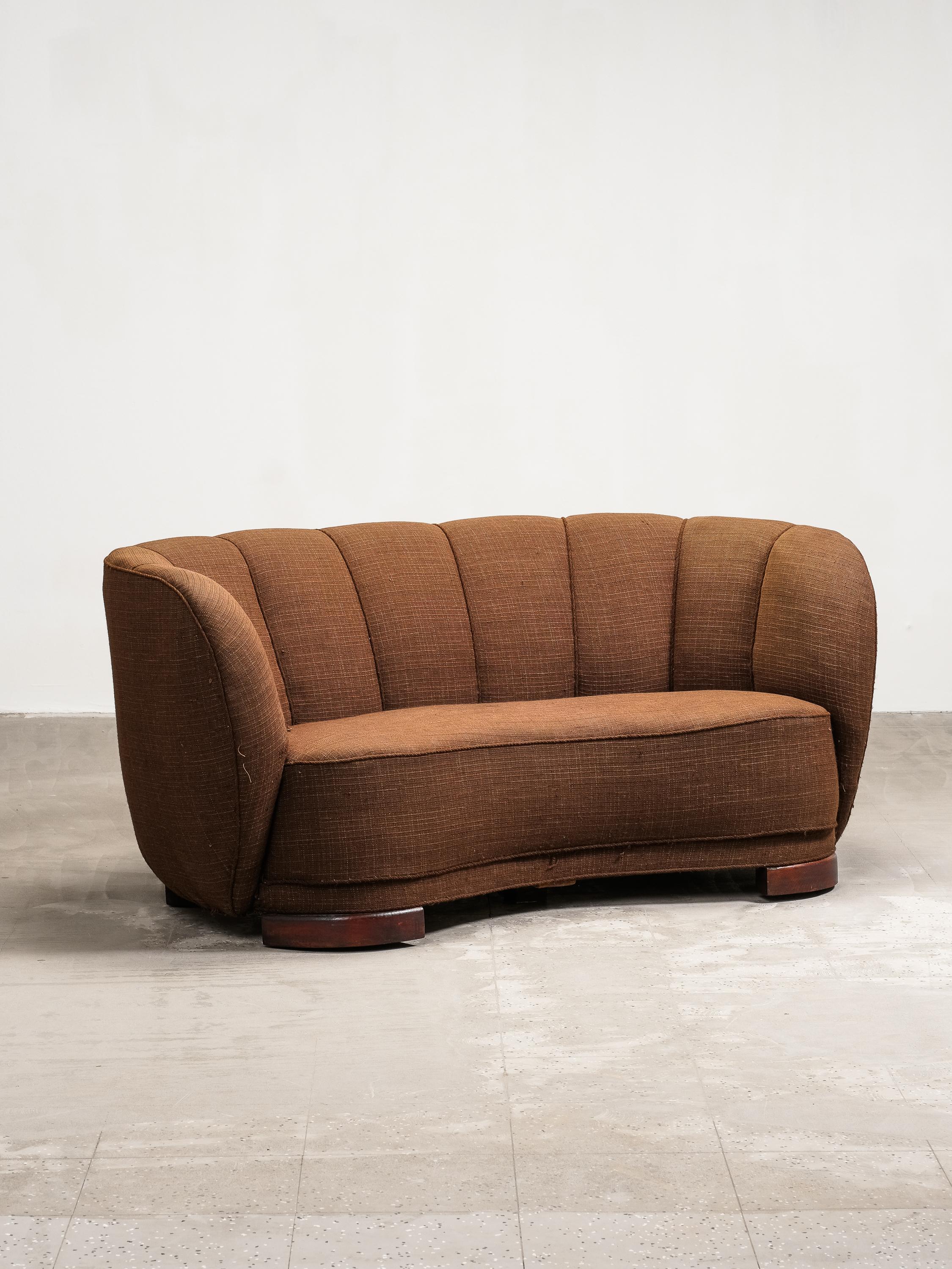 A beautifully sculpted example of Danish mid-century design, this curved sofa from the 1940s captures the refined elegance and organic lines characteristic of Scandinavian modernism. Its inviting silhouette features a gently scalloped backrest and