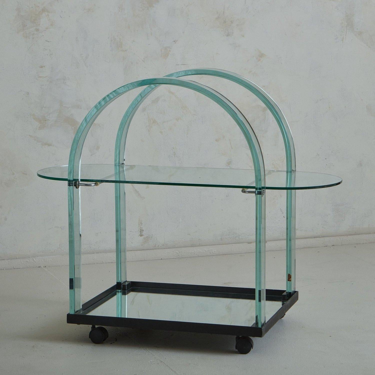 A 1980s bar cart by Italian glassmaker FIAM. This bar cart features a curved glass frame in a gorgeous aqua hue with an oblong glass shelf, which sits on curved chrome supports. It has a black metal base with a mirrored interior and stands on