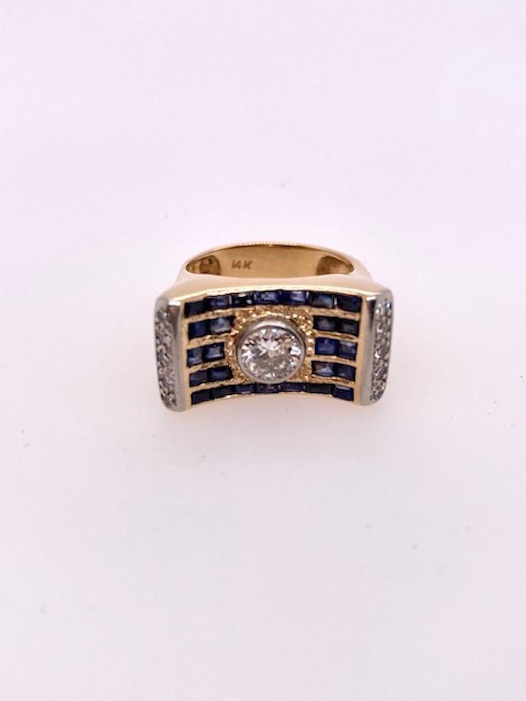 Striking diamond and sapphire ring.  Unusual design with contoured center and upsweep sides which highlight a bezel-set round brilliant cut diamond, weighing approximately .65 cts (G/H color, VS clarity).  Square step and baguette cut sapphires,