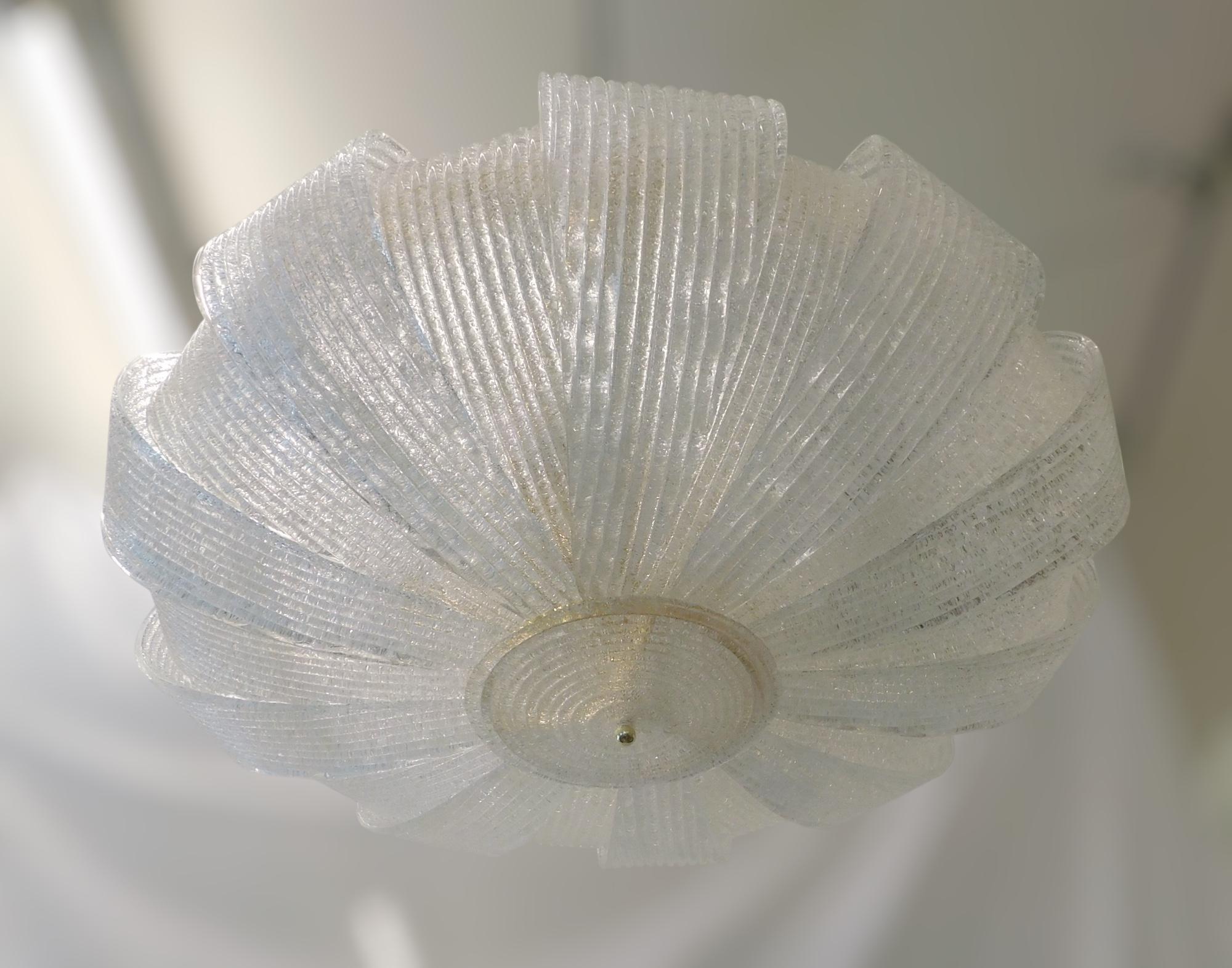 Grand encastré italien composé d'abat-jour courbes en verre de Murano soufflé à la main avec la technique de la graniglia pour produire un effet texturé granuleux, monté sur une monture en métal doré / Made in Italy
9 lampes / type E26 ou E27 / max