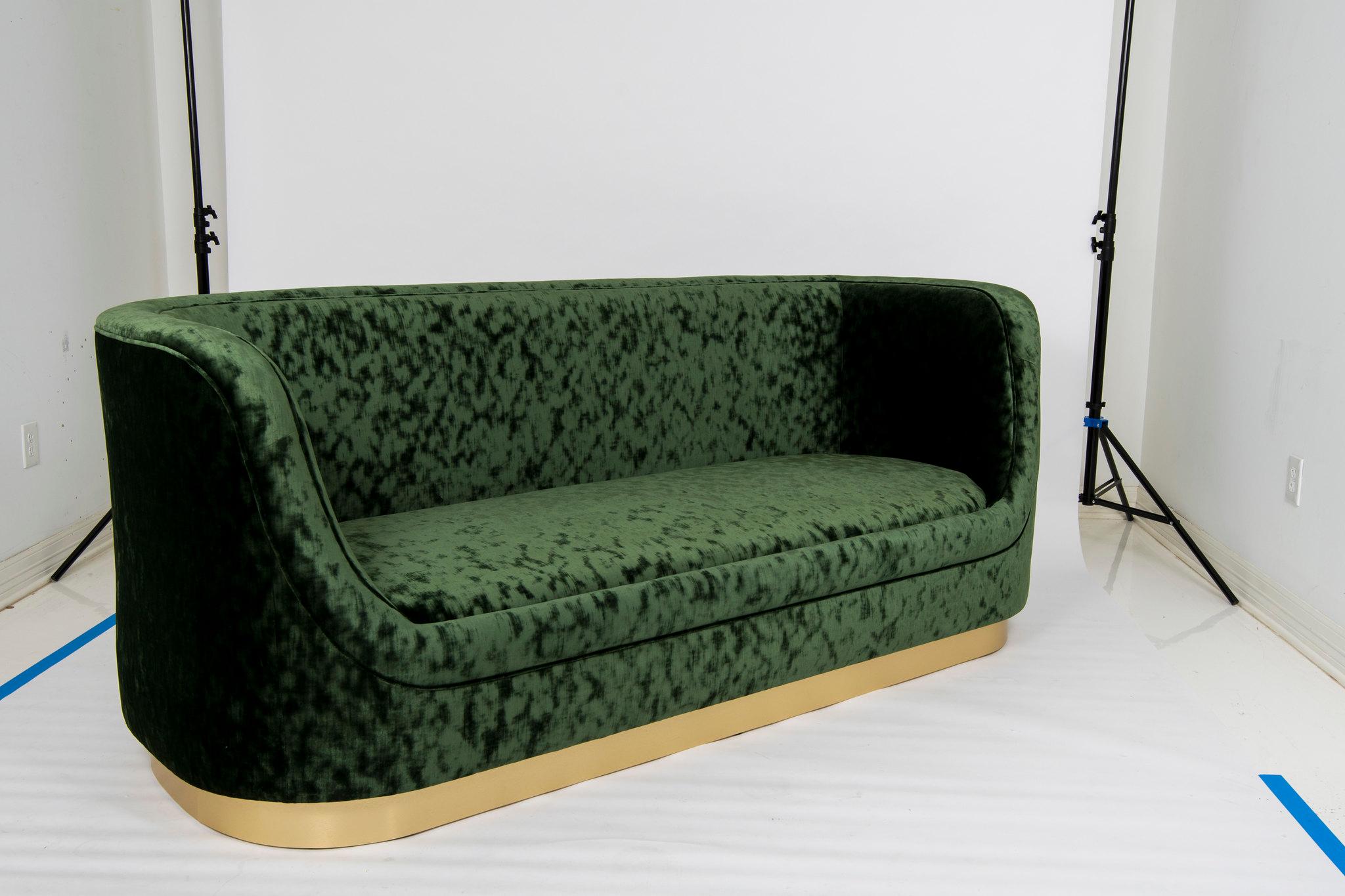 A chic curved tuxedo style sofa with brushed brass base. This stylish tight seat custom sofa is upholstered in a striated forest green velvet with frame construction of kiln dried hardwoods and eight way hand tied coiled springs.