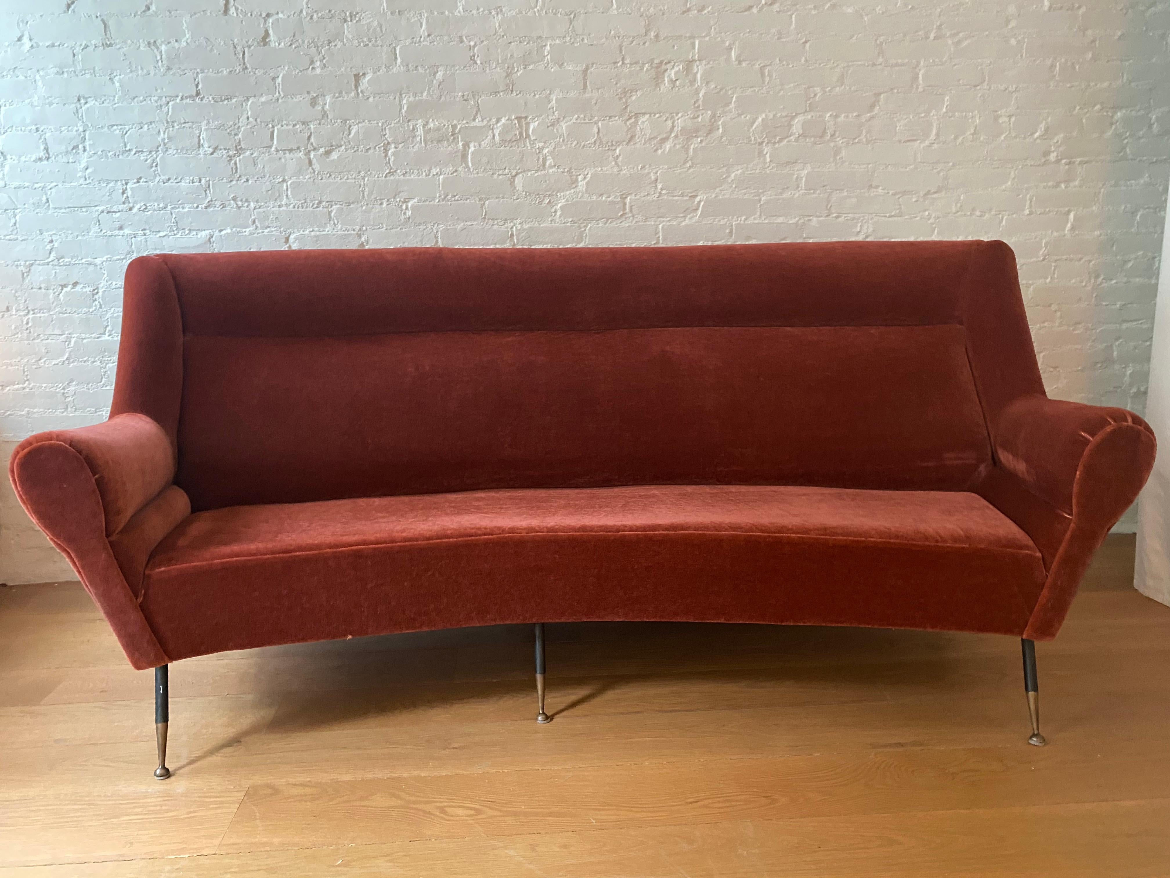 Gracious long curved 1950s Italian sofa by Gigi Radice. With curved shoulders and arms, the sofa body rests on tapered black metal legs with brass tipped feet. Legs attached to iron supports on sofa bottom. Luxurious mohair upholstery has some wear