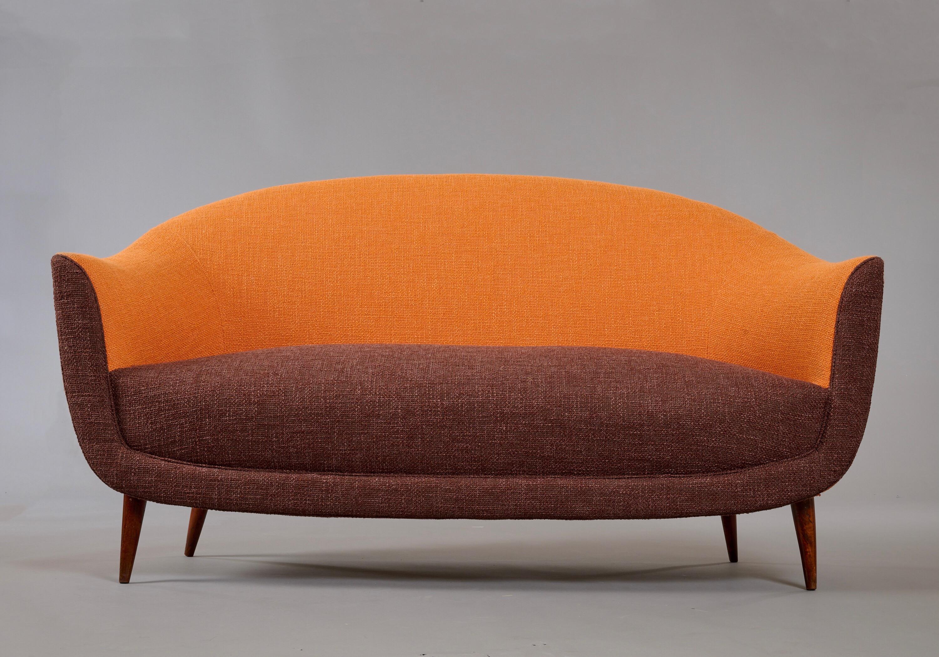Italy, 1950's.

A charming curved sofa in the style of Federico Munari, with a comfortable, high sloped back and rounded, elegantly tapering arms, raised on conical wood legs. Newly reupholstered in contrasting burnt sienna and chocolate cotton