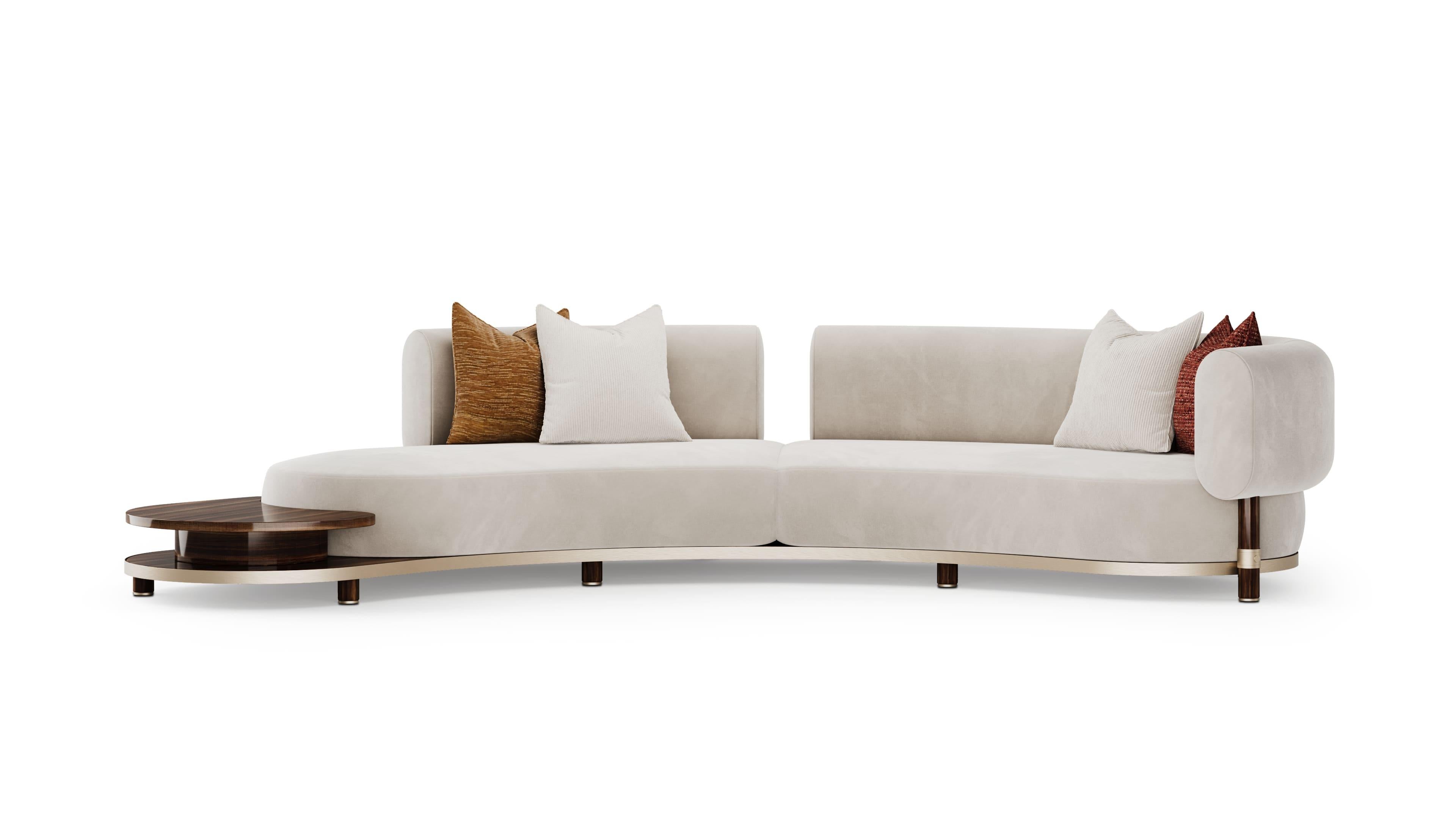 Blosse Sofa embodies fluid elegance with its generous, curved silhouette and soft cream upholstery. Designed to seat over four comfortably, it offers both spaciousness and refinement for sophisticated interiors. A seamlessly integrated walnut side