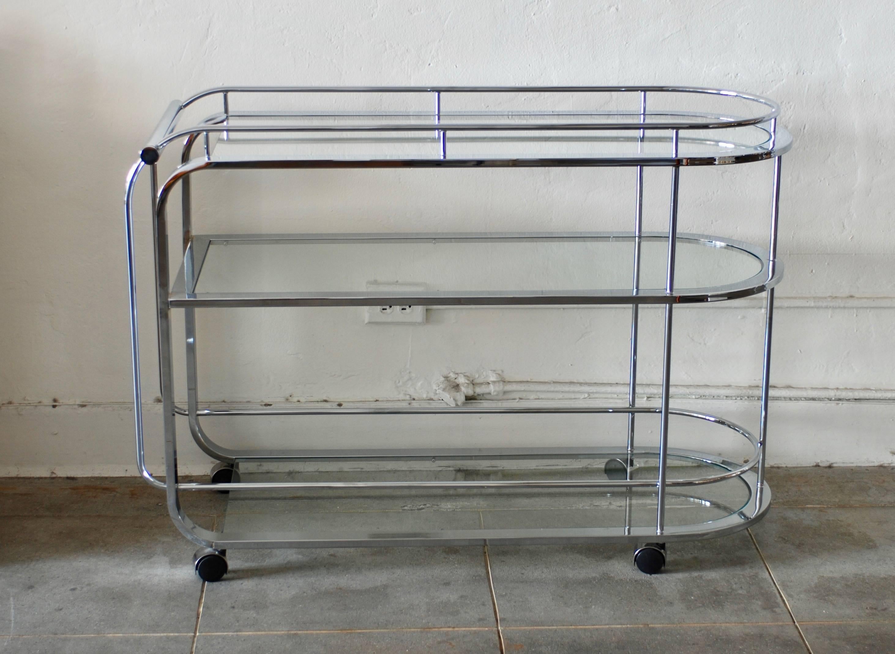 A sleek moderne style bar cart with nice curves. The bar cart or tea trolley has three-glass shelves. The length of it gives ample serving room. The last photos of the vintage glassware and barware is for scale and demonstration purposes and is not