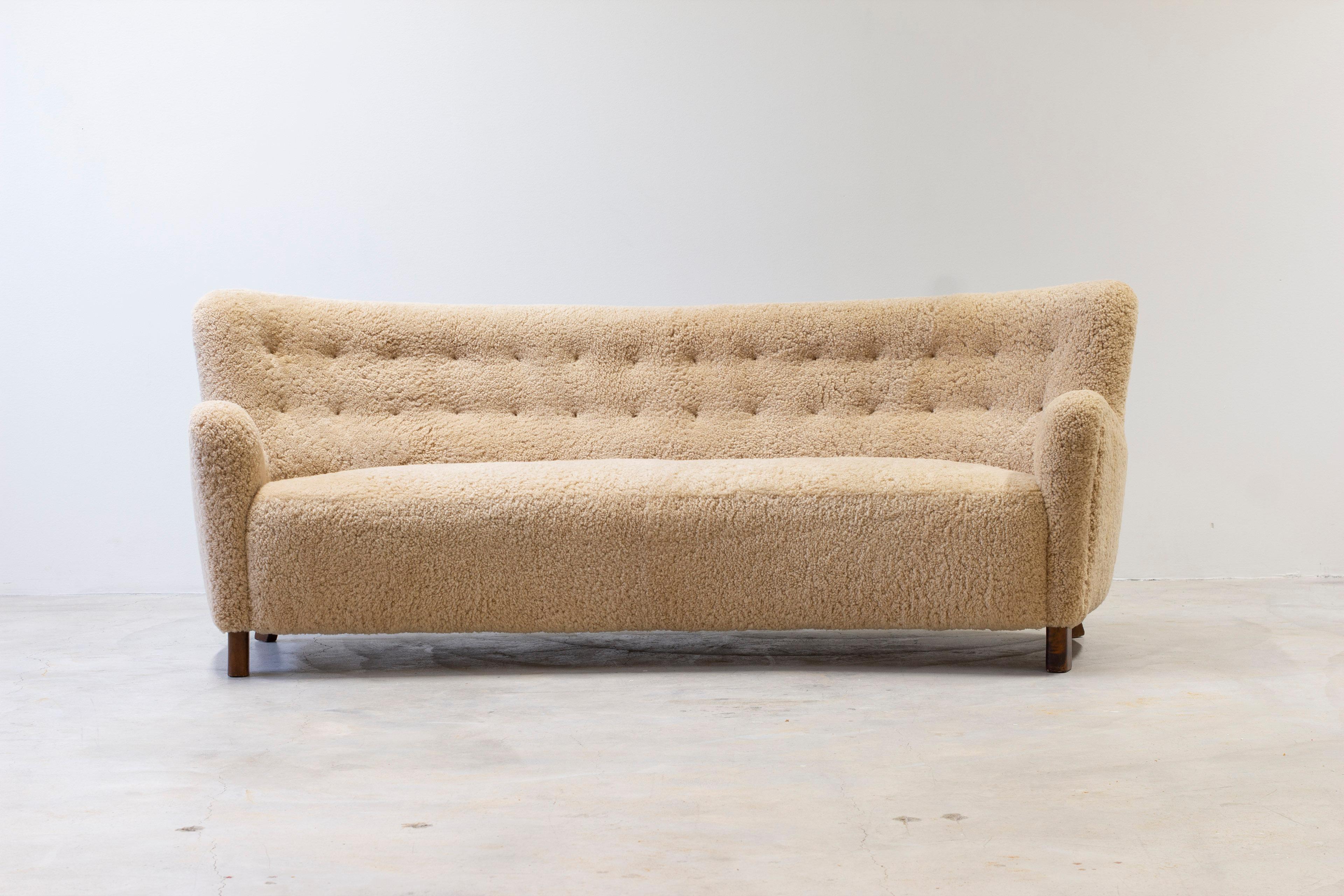 Curved four seater sofa model 1669 by Fritz Hansen. This curved model later production on license by FDB (Fritz Hansen design) from the 1950s. Reupholstered in beige sheep skin with dark stained birch legs. Exceptionally good upholstery work made