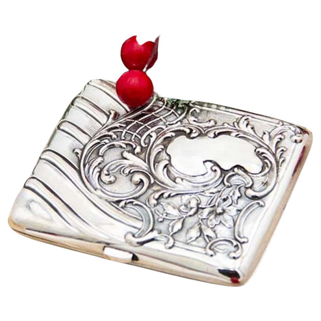 Curved silver cigarette case with engraved wreaths around monogram