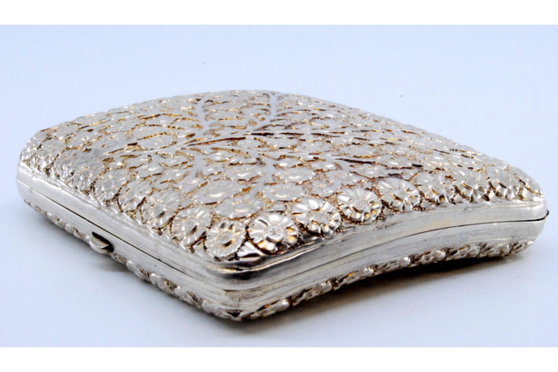 Description: Curved silver cigarette case with flower and branch reliefs. Metal: Silver. Origin: Portuguese. Brand: Eagle Head. Weight: 96.37 grams. Dimensions: 8.5x7.4cm. Content: 833/1000. Assay Mark: Yes, between 1938 and 1984. Additional