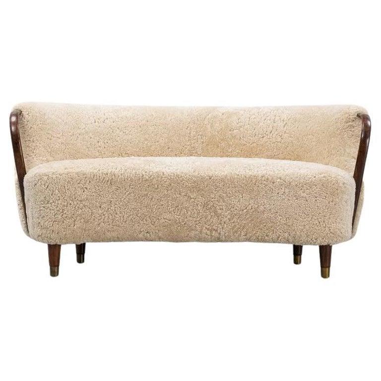 A curved sofa attributed to Viggo Boesen with new sheepskin upholstery and stained beech tree armrests.

Superb banana shaped loveseat or settee with open armrests designed and made as Model 96 by N.A. Jørgensens Møbelfabrik in 1954-1955. N.A.