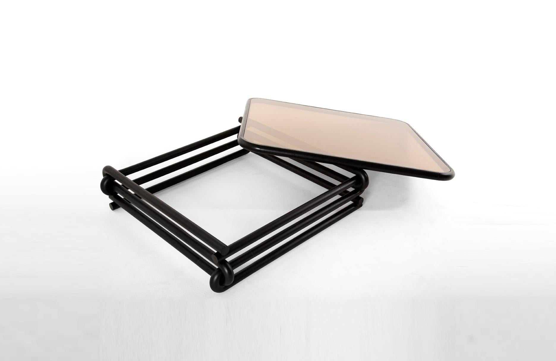 Eight U-shaped curves interlock each other to create a square base structure. A series of bevels etched into the table help to emphasize the attaching points. A double pane bronze glass top is bordered with eased hardwood edges. Café Con Leche is