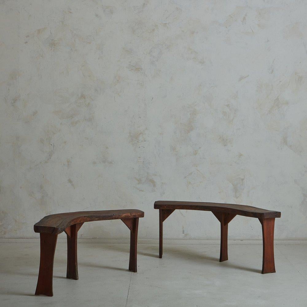 A vintage French bench constructed with stained oak wood in a rich mahogany hue. This bench has beautiful, time honored wear and features a curved seat with three carved legs. Sourced in France, 20th Century. Two Available; Priced Individually.