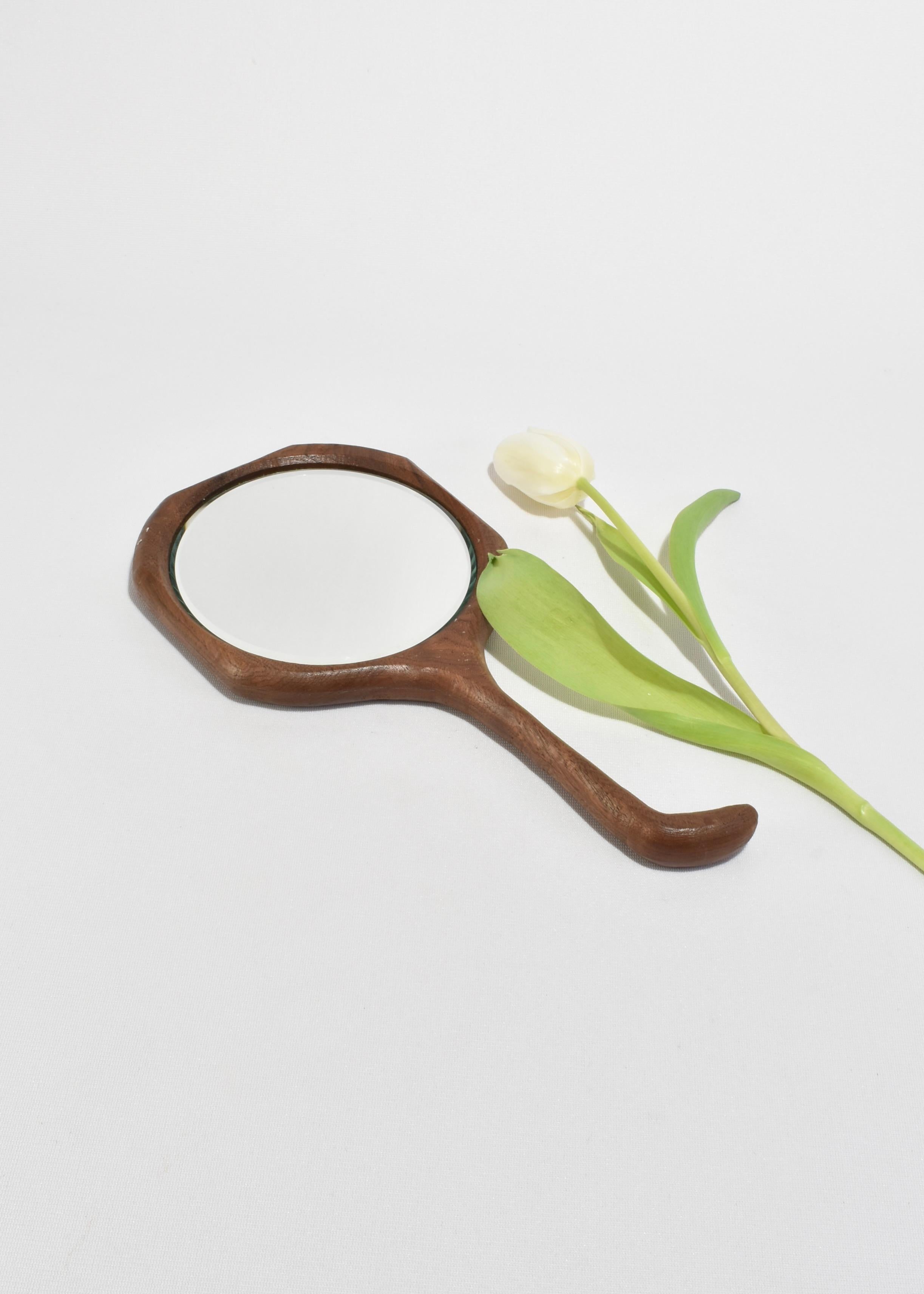 Vintage hand-carved wooden hand mirror with a curved handle and spiral detail on the backside.