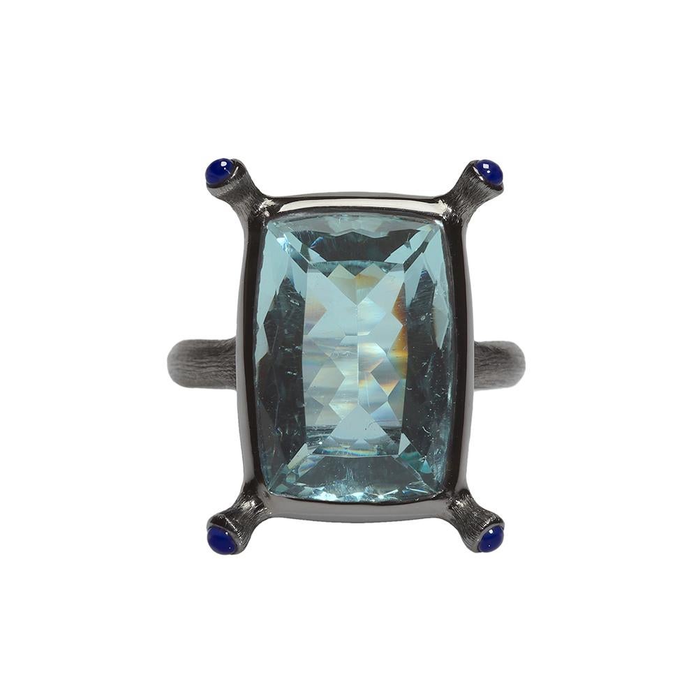 This stylish ring features a vibrant rectangular cushion shape Aquamarine set in 18 karat blackened gold with extended prongs inventively set with cabochon blue sapphires. The setting creates a tender romance between high-karat blackened matte