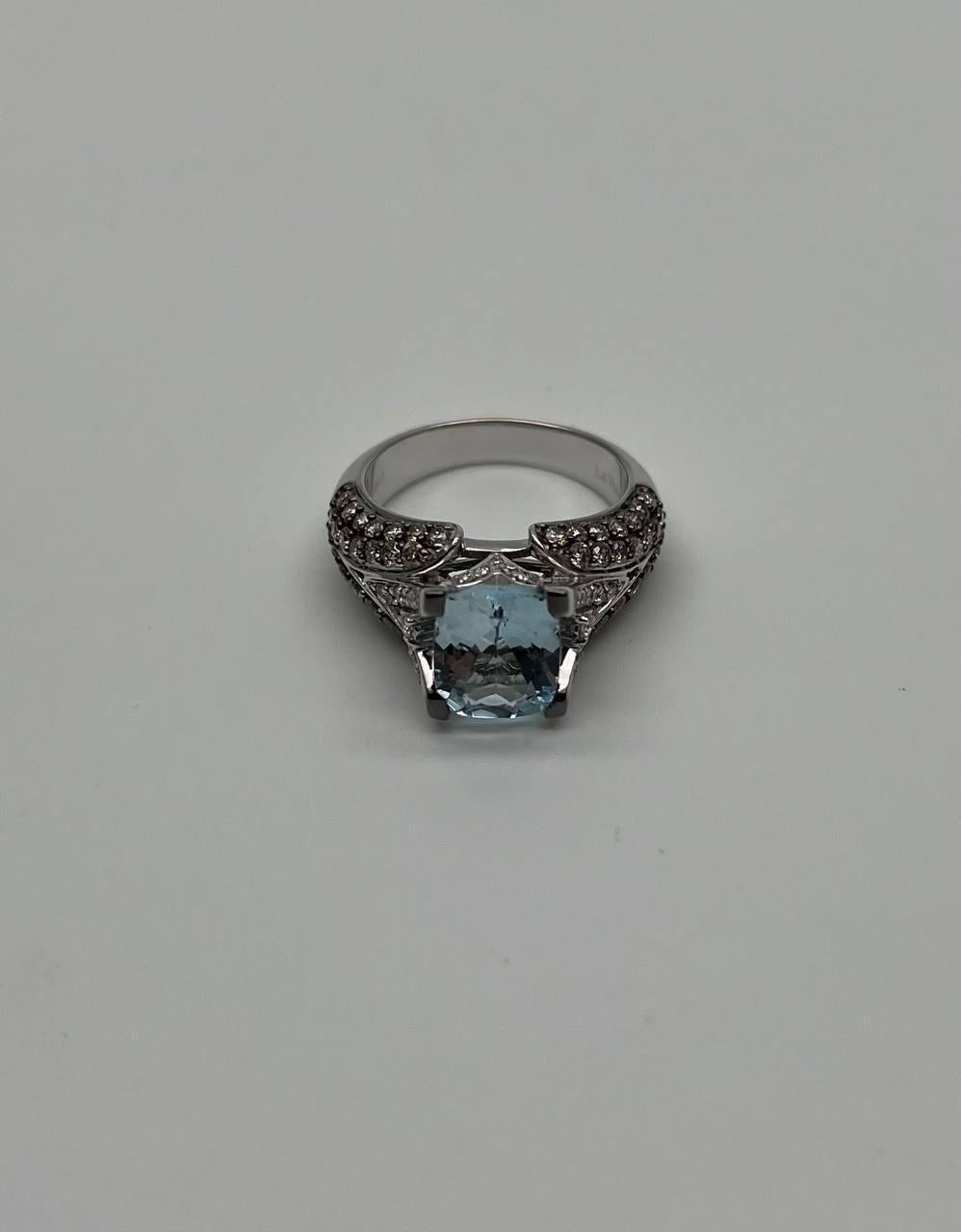 Discover the allure of our exquisite ring, a masterpiece of modern elegance.

Crafted with precision, this ring features a captivating central cushion-cut aquamarine, its light blue hue radiating sophistication. The band is adorned with a series of