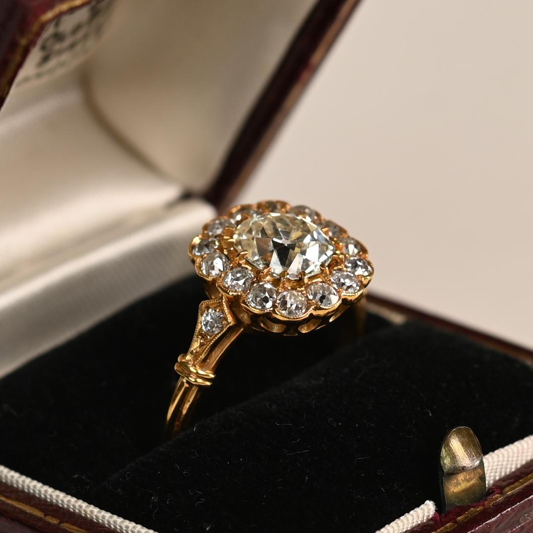 Cette exquise bague de fiançailles antique en forme de grappe met en valeur un diamant de taille coussin en son centre, pesant environ 1,3 carat. De couleur K et de pureté VS1, le diamant présente un éclat captivant qui reflète le charme d'une
