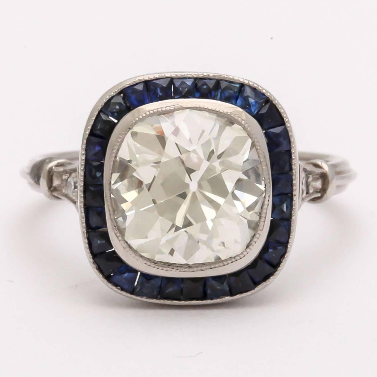A stunning 2.60ct VS-1 J/K vintage cushion cut diamond is surrounded by French cut natural sapphires flanked by two smaller brilliant cut diamonds and set into a handcrafted custom designed mount. Appraisal available.