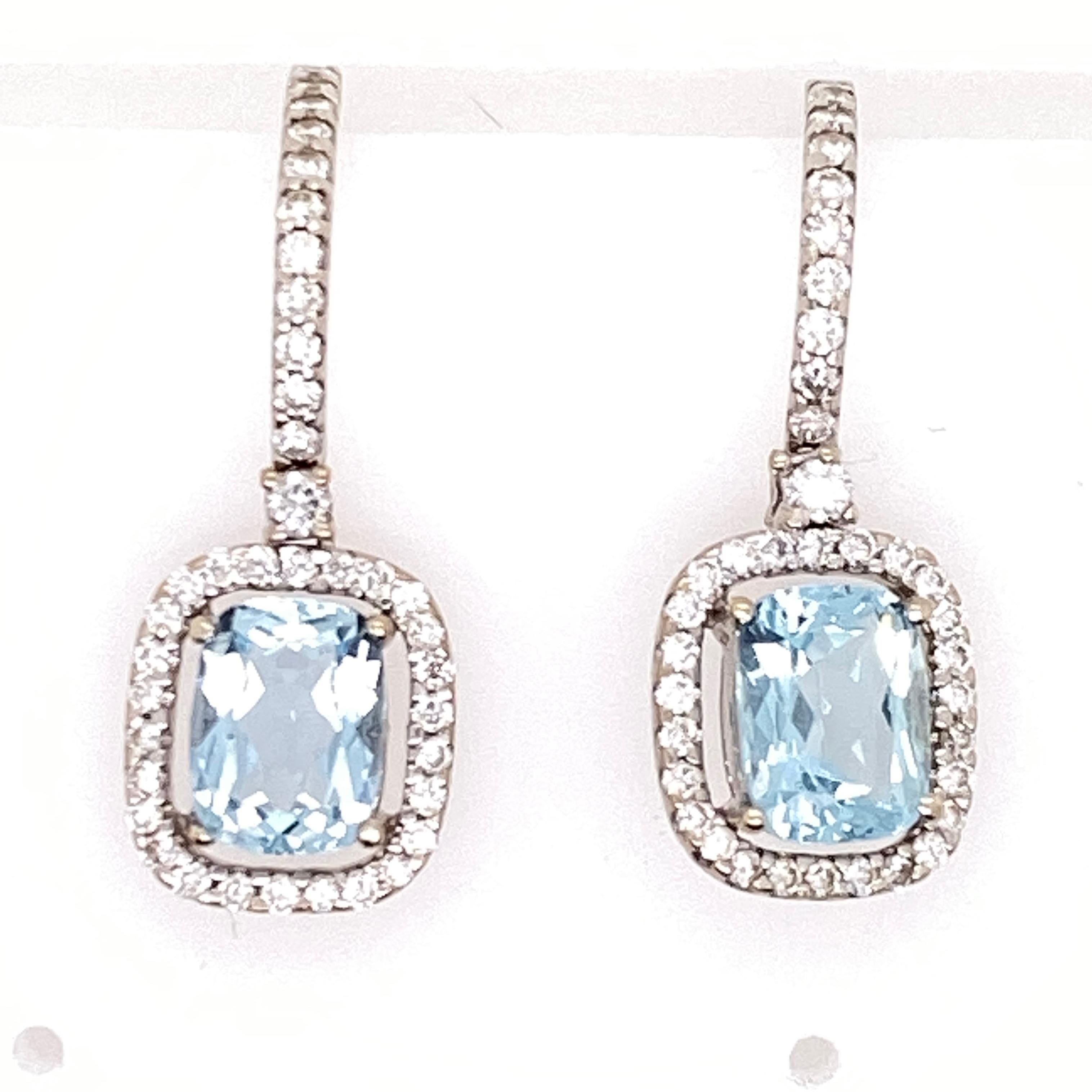 Aquamarine diamond drop earrings fashioned in 14 karat white gold. The two cushion cut aquamarine gemstones (1.50 CTW) are surrounded by 74 round brilliant cut white diamonds (.50 CTW). The earrings measure 1.0 inch in length and .40 inches in