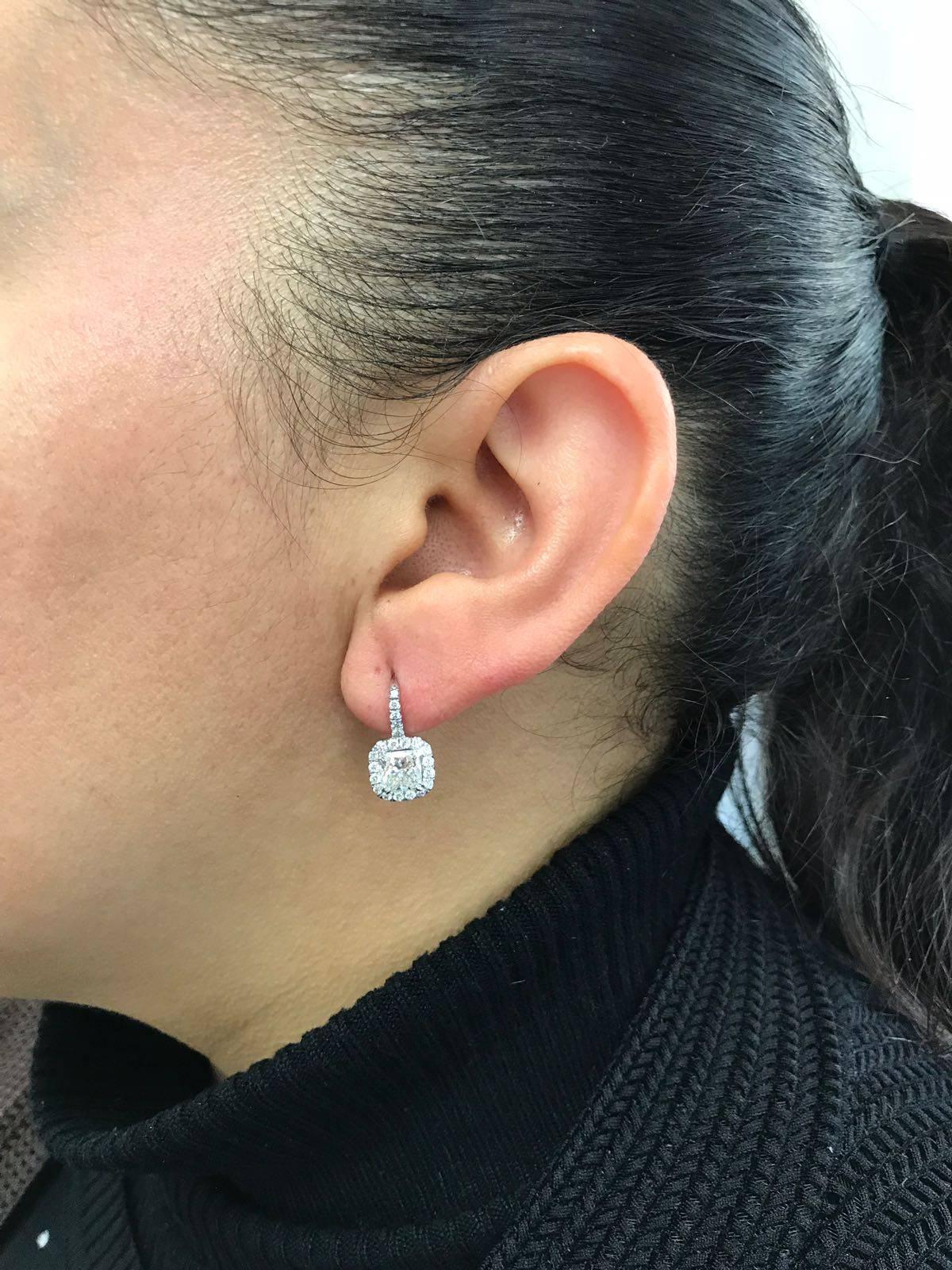 Classic halo drop earrings featuring GIA certified 1.03 carat and 1.05 carat cushion cut diamonds on each earring. GIA certfied each diamond as H color, SI1 clarity and I color, VVS2 clarity respectively. Each cushion cut diamond is surrounded by a