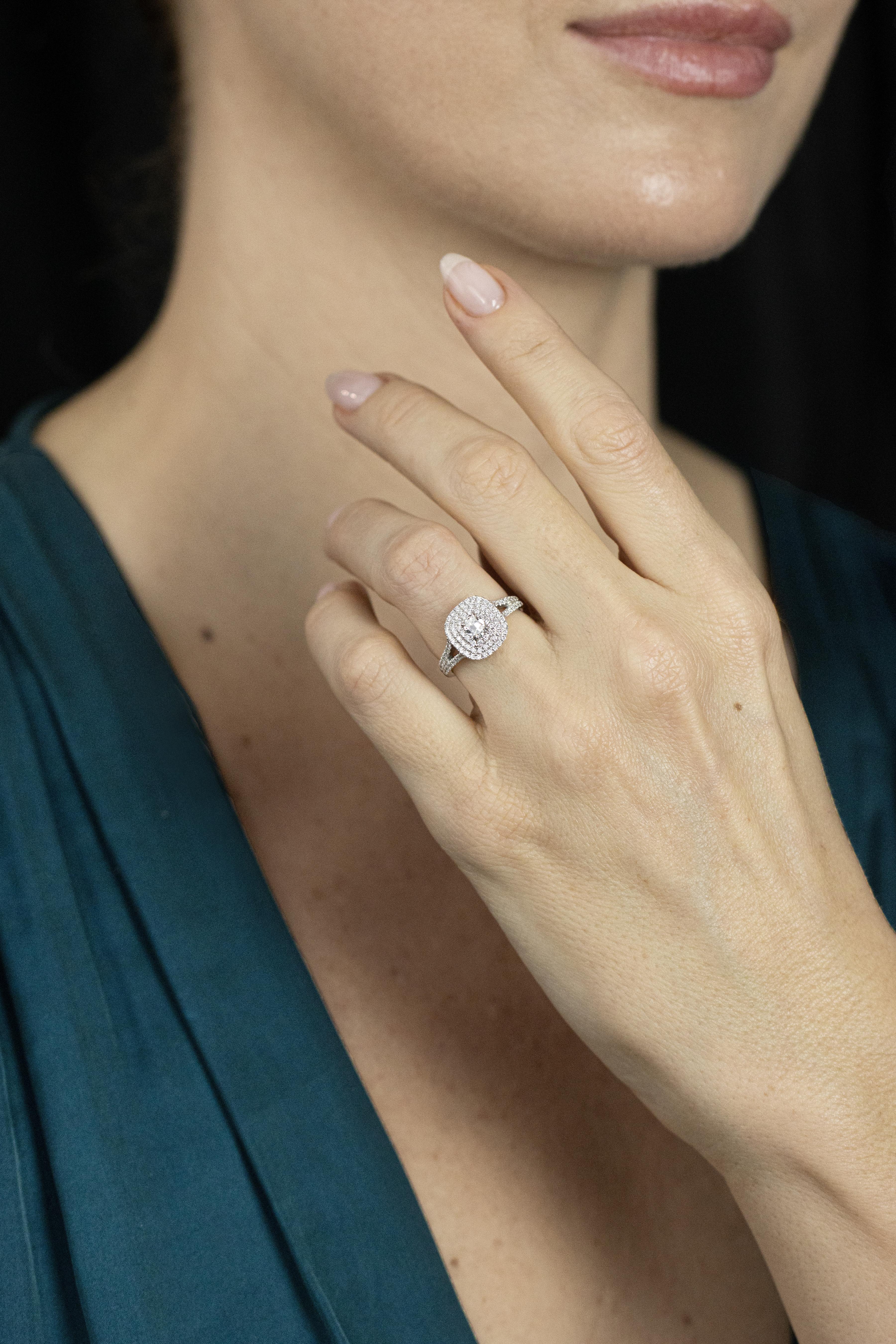 A unique engagement ring, showcasing a 0.35 carat cushion cut diamond with E color and VS clarity, set on a four prong setting. Surrounded by a triple halo of round brilliant cut diamonds and accented by a diamond encrusted split-shank in a