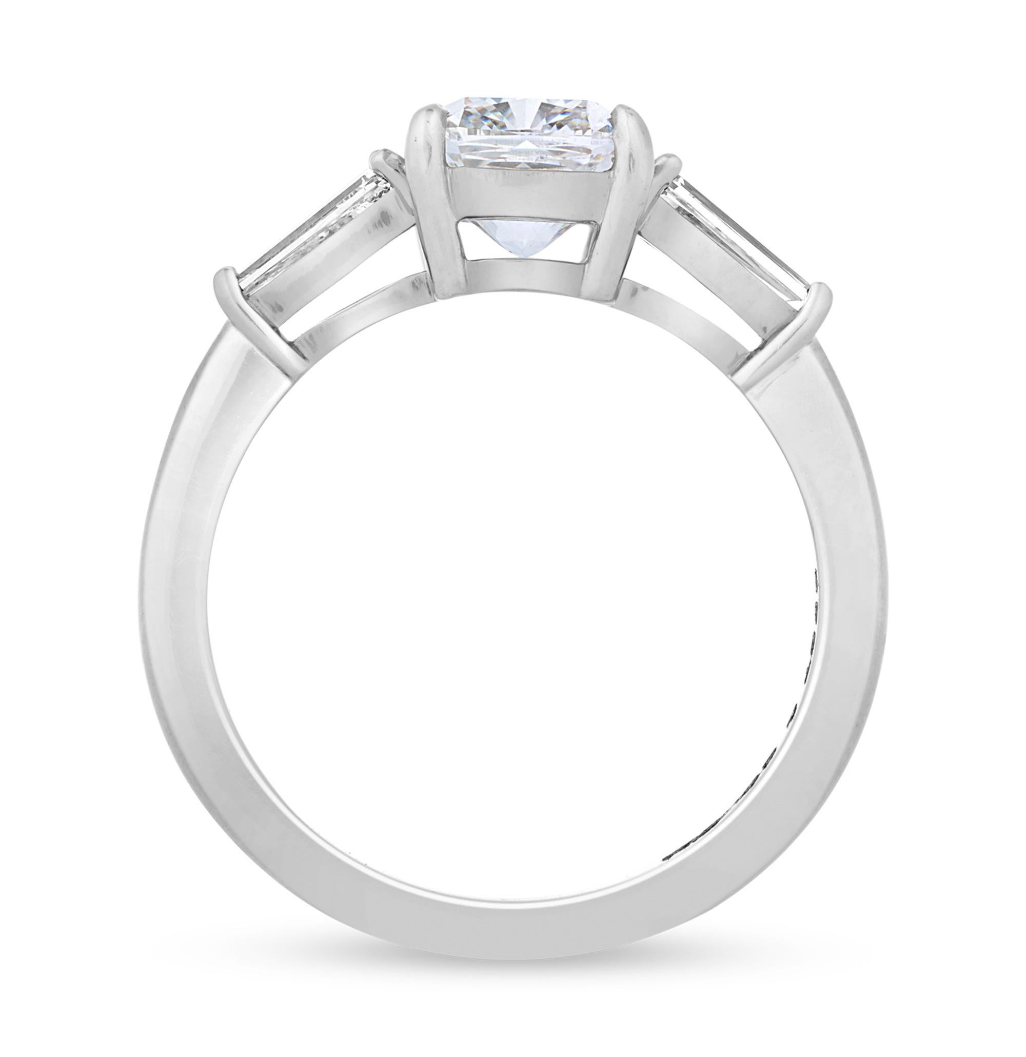 Este llamativo anillo de diamantes exhibe un diamante blanco talla cojín de 1,61 quilates como brillante pieza central. Certificada por el Instituto Gemológico de América (GIA), esta impresionante piedra alcanza el extraordinario grado de claridad
