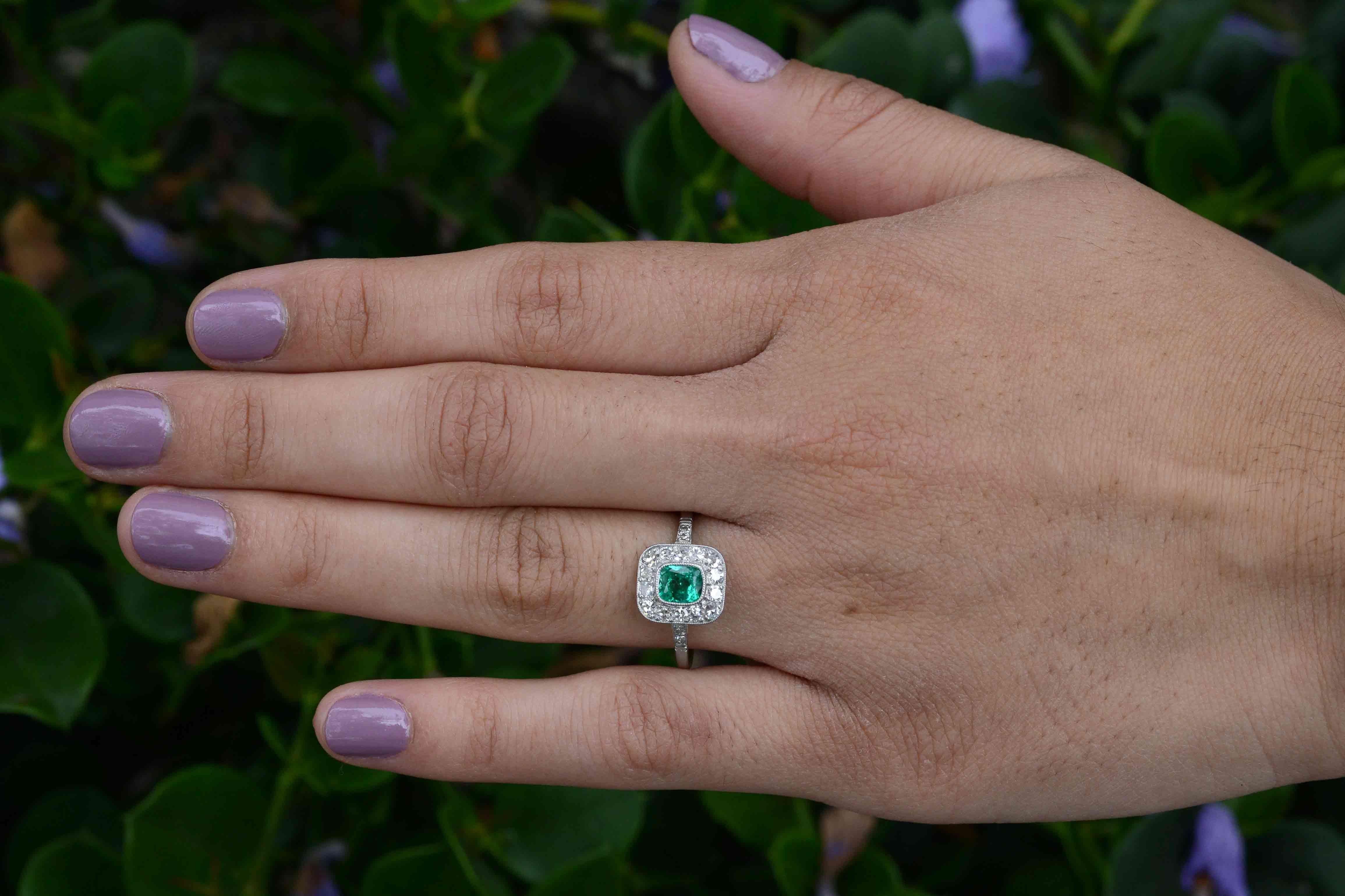 You will not be able to stop staring at this Art Deco engagement ring. Centering on a 3/4 carat cushion cut Colombian emerald of the most crisp and lively green. The strong, low, platinum bezel setting with it's vintage milgrain detailing and