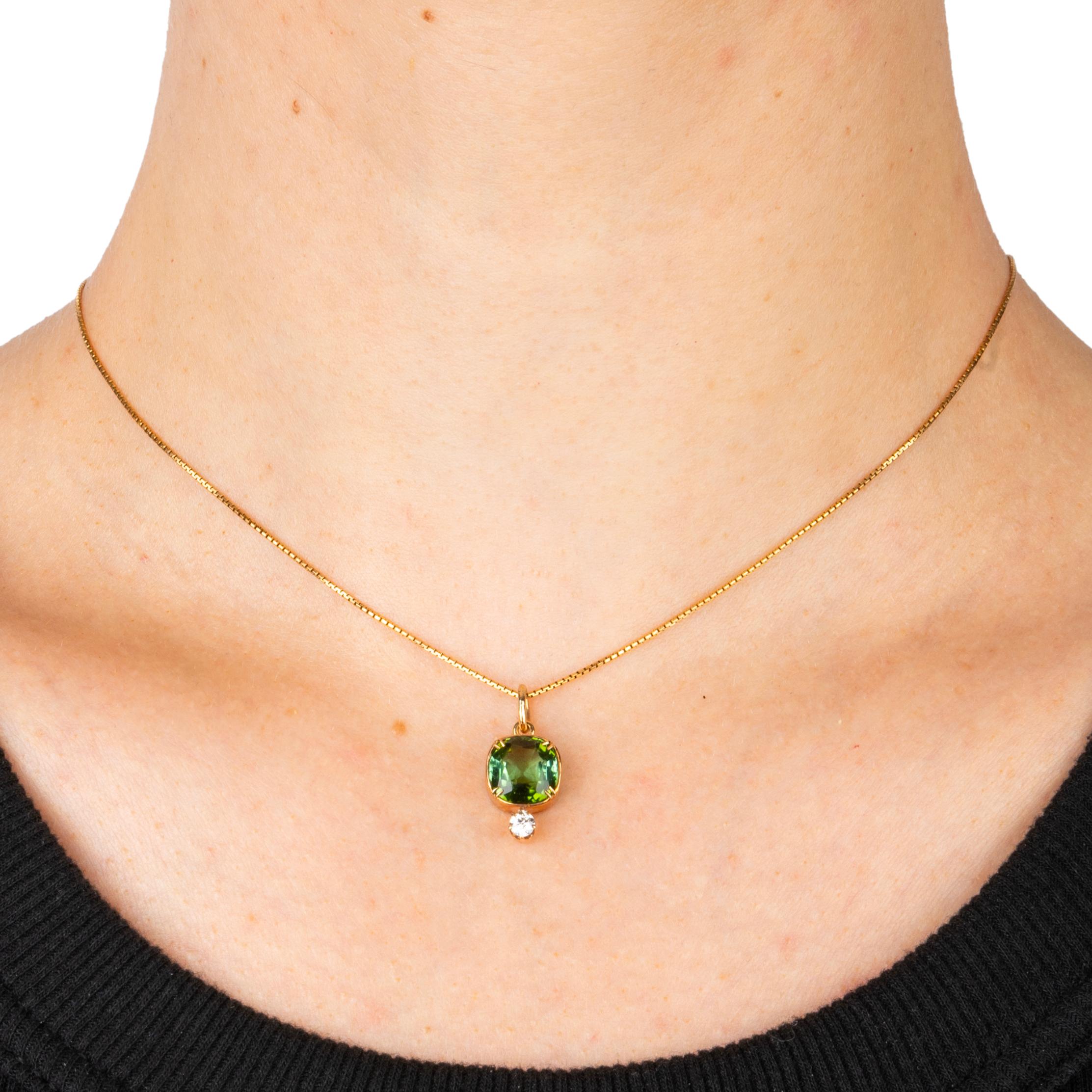 Este hermoso e intemporal colgante de oro amarillo de 14 quilates de los años 30 tiene engastada en bisel una deliciosa turmalina verde en forma de cojín sobre un brillante diamante de talla europea antigua engastado con un anillo ovalado de