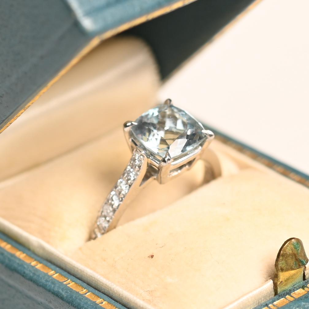 Este exquisito anillo exhibe una aguamarina natural vibrante y profundamente saturada de aproximadamente 1,50 quilates, su cautivador tono azul recuerda a las aguas más claras del océano. La piedra central está bellamente complementada por una serie