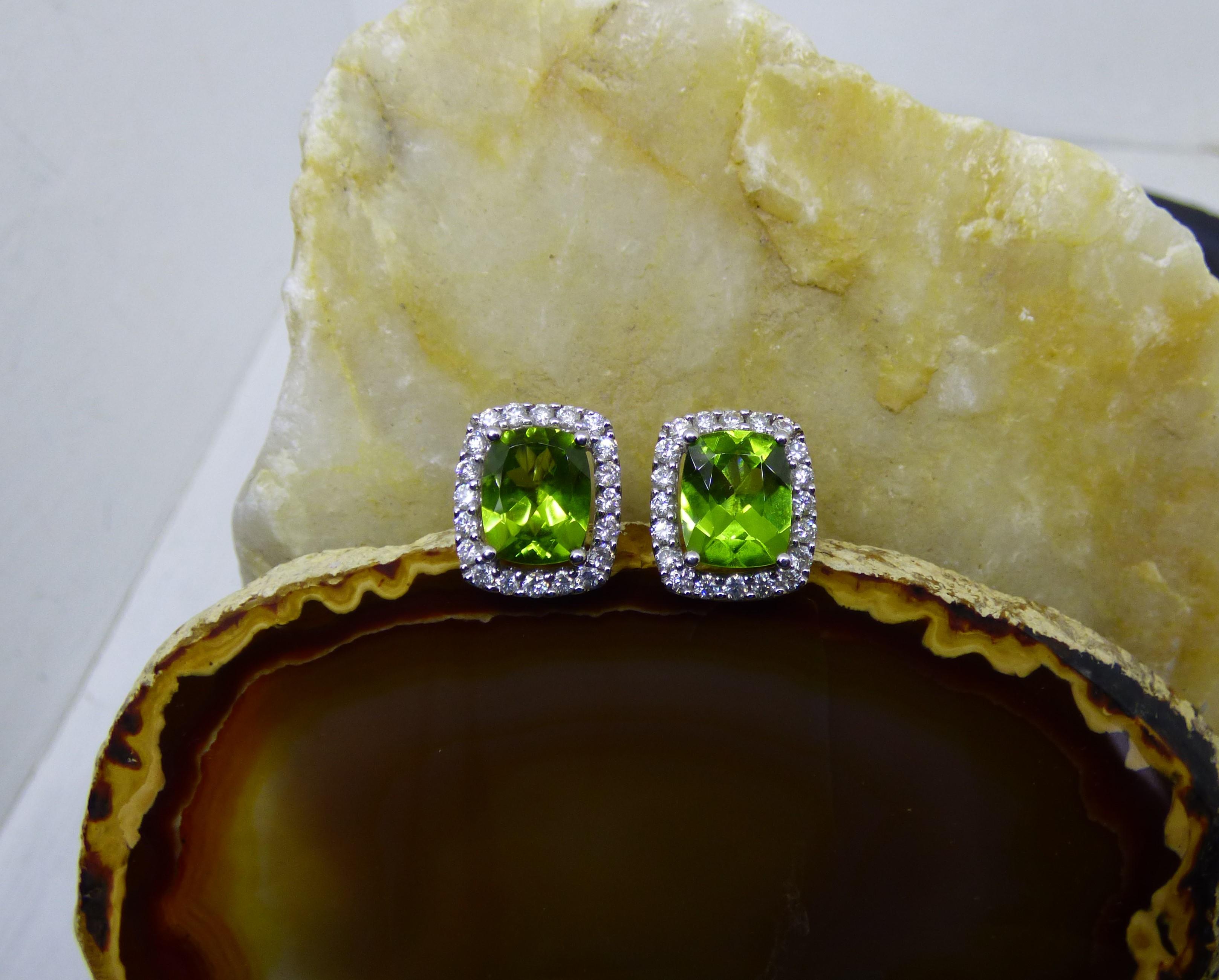 Bright clean colourful Peridot star in these earrings. The 11X9mm cushion cut stones have a total weight of 5.6ct.  The Peridot are surrounded by 20 diamonds with a total Diamond weight of 1.13ct. The earrings are handmade in 18K white gold and
