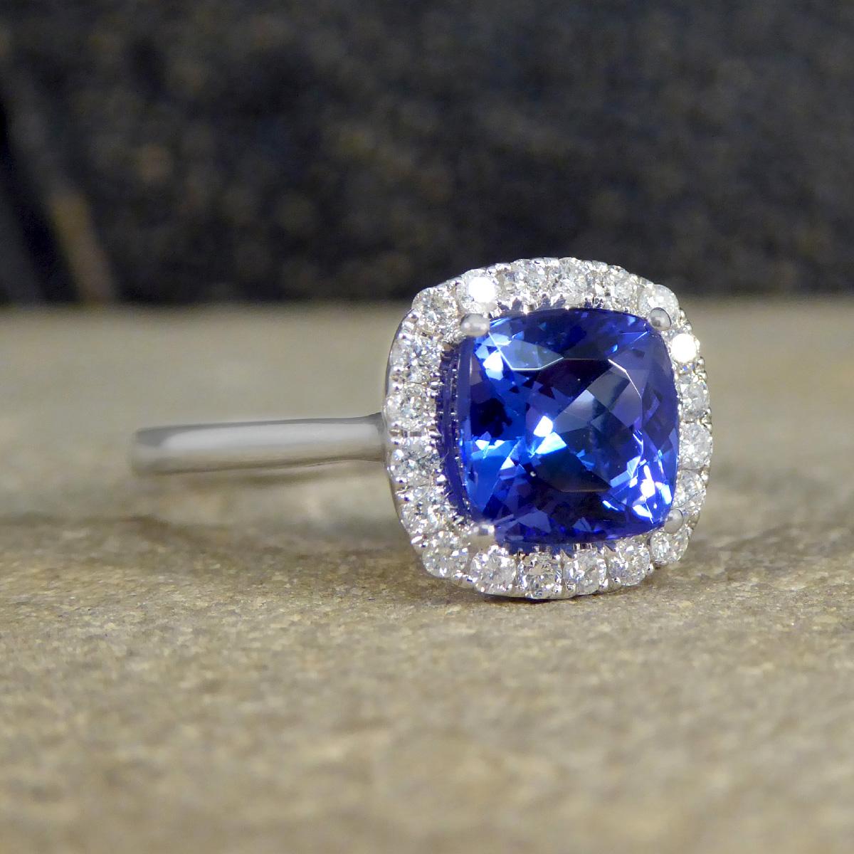 This gorgeous and alluring 1.87ct Cushion Cut Tanzanite and Diamond cluster ring is a masterpiece of elegance and allure. At its heart sits a mesmerising cushion cut tanzanite, renowned for its deep and captivating blue-violet hue, symbolising