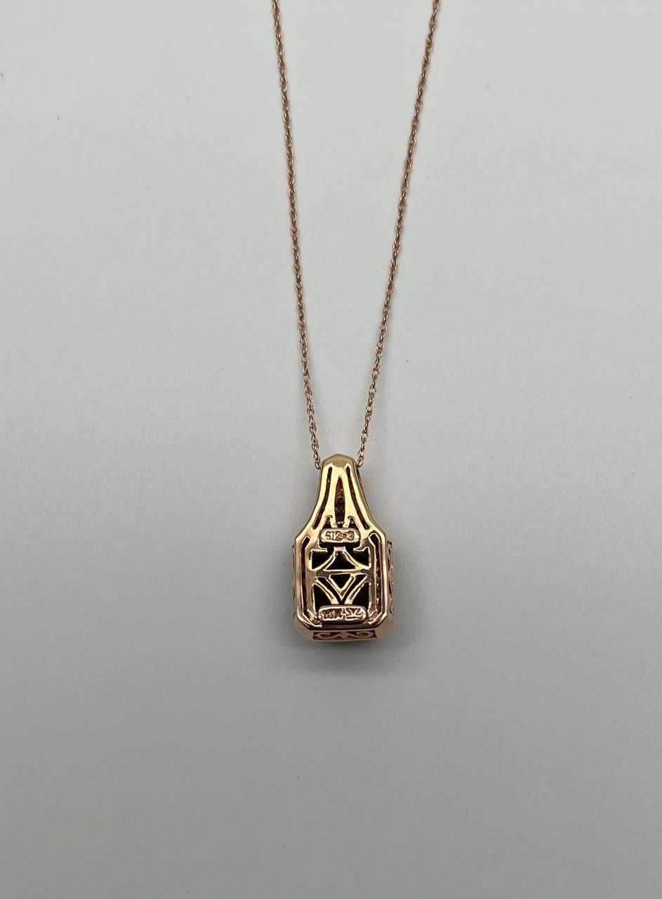 A striking pendant necklace featuring a radiant red garnet set in a rectangular frame, adorned with a halo of sparkling diamonds . The pendant is suspended from a delicate chain, crafted in a warm-toned metal. 14K Rose Gold.