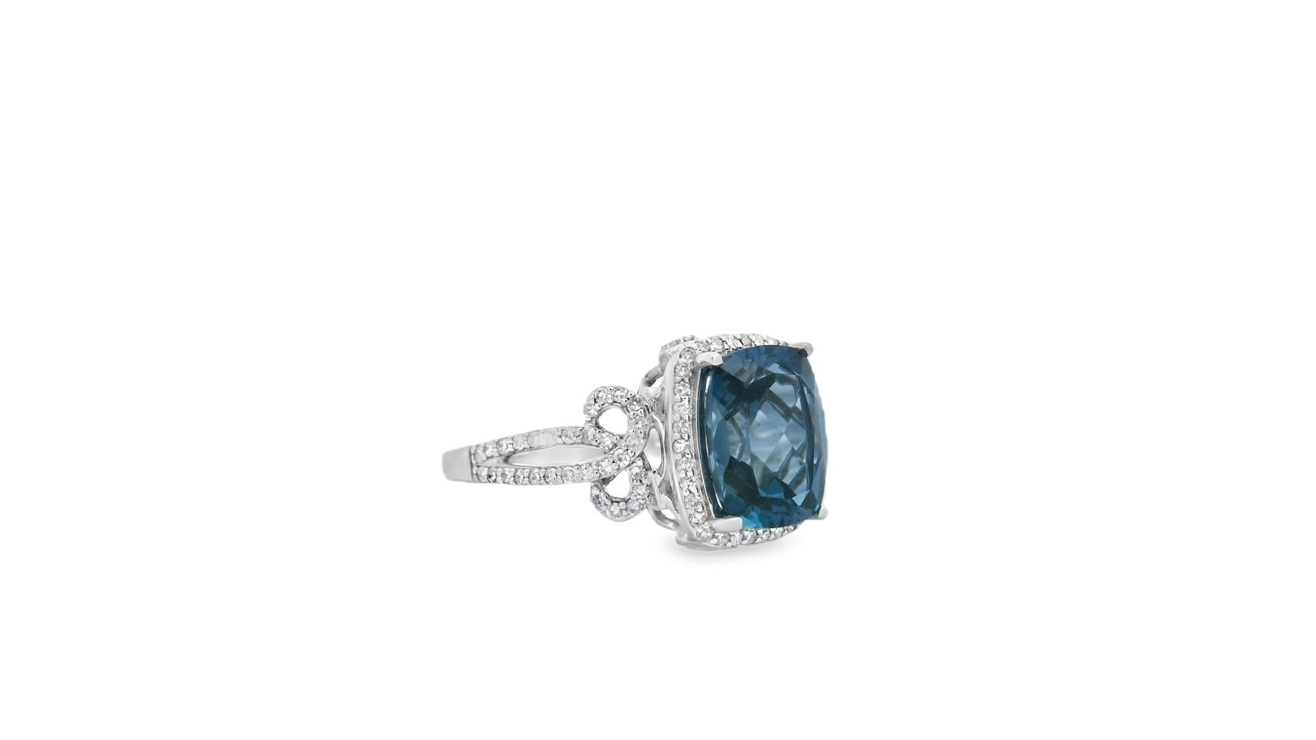 This elegant cocktail ring features a richly hued 3.65-carat cushion-cut London blue topaz framed in a glittering diamond halo and mounted in 14K white gold. The 10x8mm center stone displays a deep oceanic blue with remarkable clarity, set in four