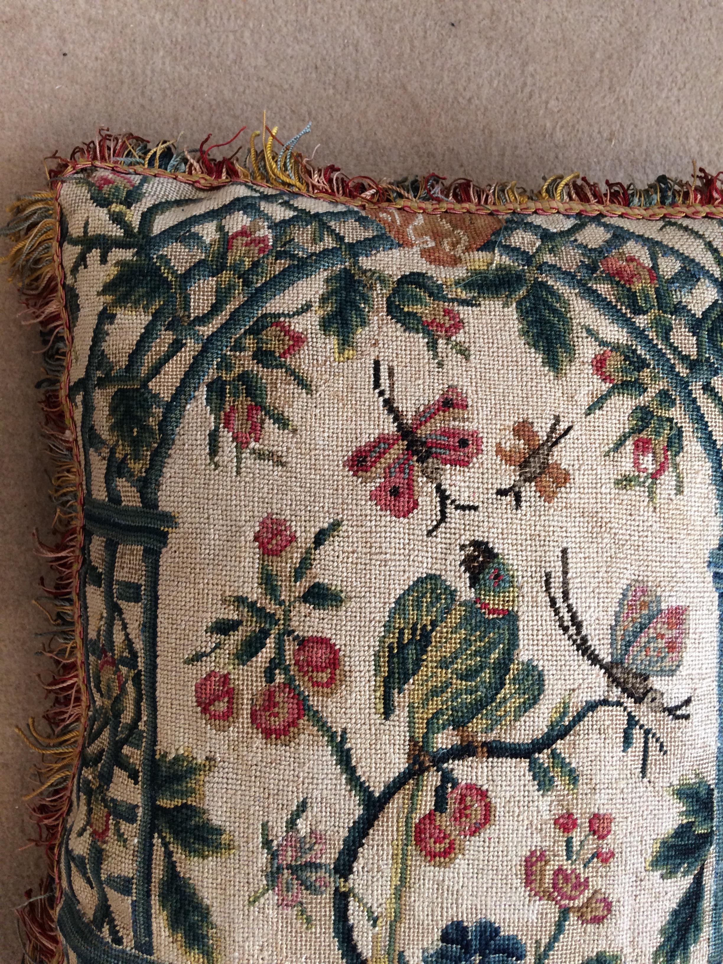 A cushion of late 18th century French needlework with a green parakeet on a white background with a trellis in the background.