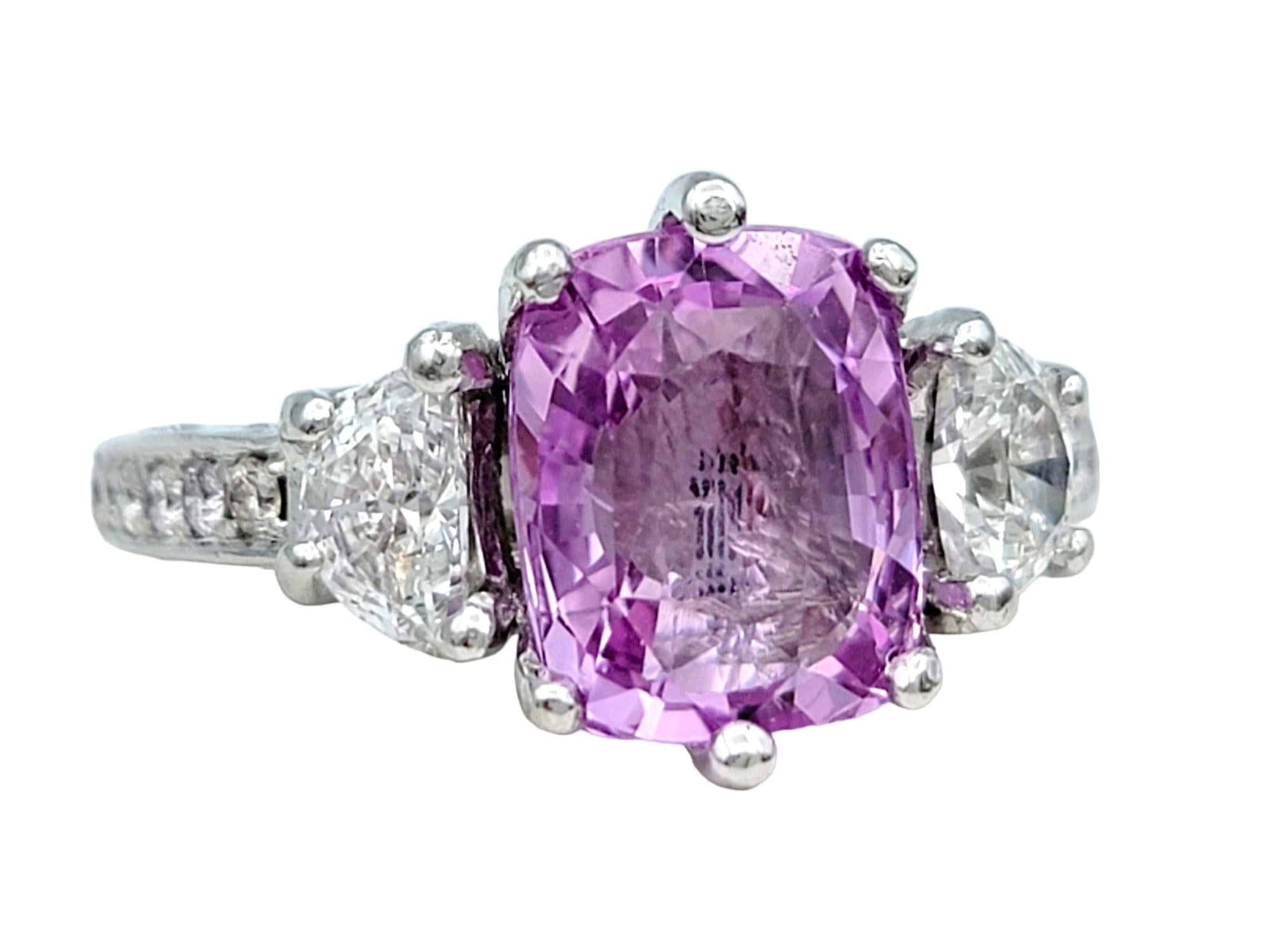 Ring Size: 5.75

This exquisite three-stone ring showcases a striking combination of elegance and sophistication. Set in platinum, the centerpiece features a captivating pink cushion sapphire, exuding a soft yet vibrant hue that immediately catches