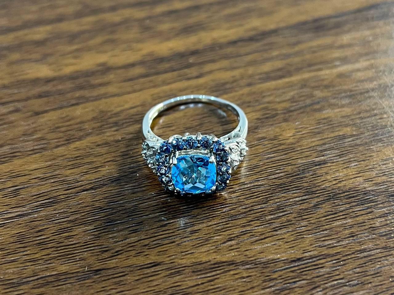 This elegant multi-stone ring is crafted in a polished 14k white gold setting. It features a vibrant blue topaz at its center, surrounded by a halo of smaller, deep blue topazes. The intricate design extends along the band with additional sparkling