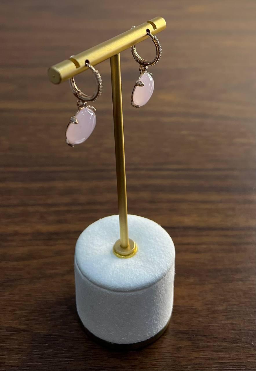 Featuring a soft pink rose quartz with a primary carat weight of 19.76, accented by delicate diamonds totaling 0.23 carats. The stones are set in 14k gold, showcasing a refined design. The earrings hang gracefully from a gold hoop, adding a touch of
