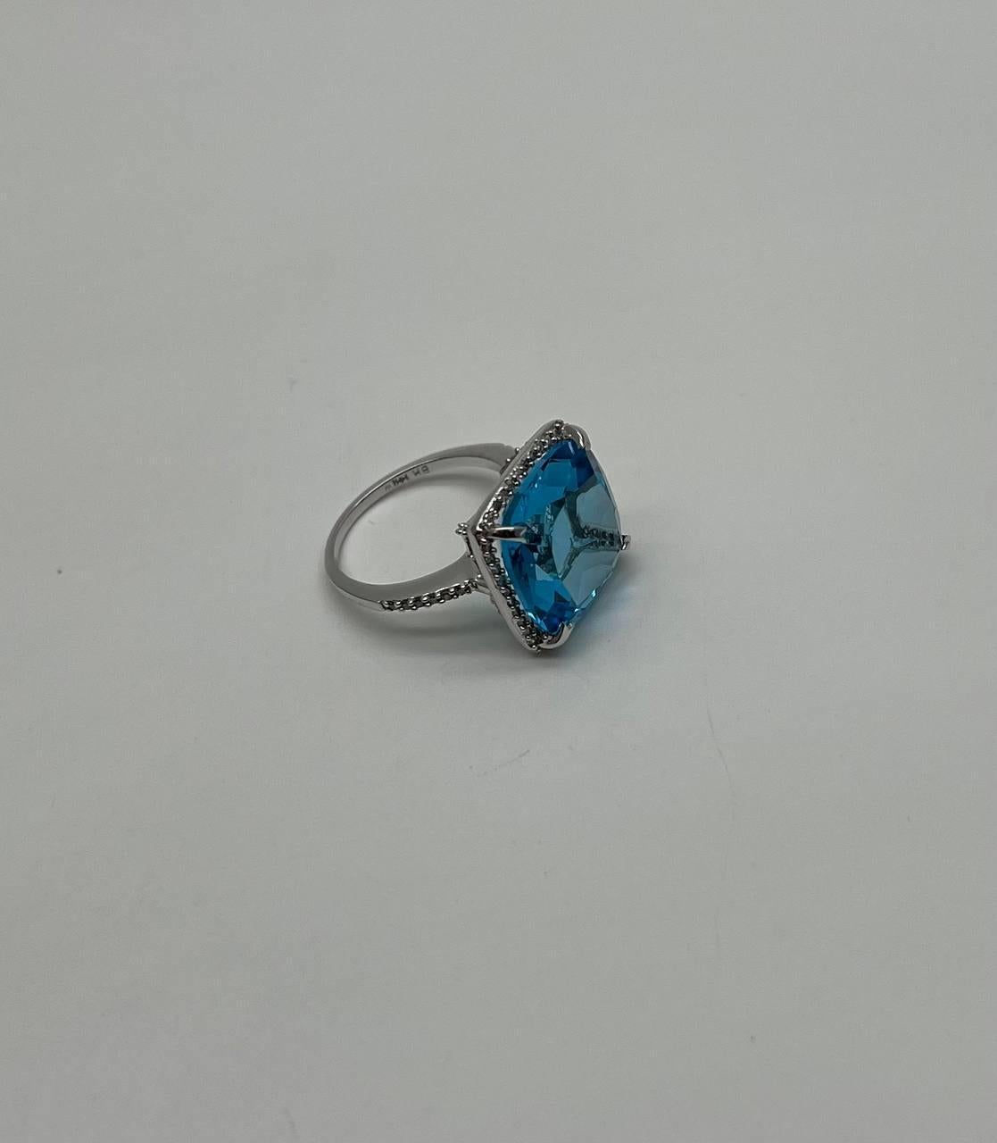 A striking Blue Topaz and Diamond Ring, featuring a captivating cushion-cut blue topaz set in a sleek white gold band, adorned with delicate diamonds. 14K White Gold. 0.33 CTW Diamonds. 14.06 Cts Swiss Blue Topaz.