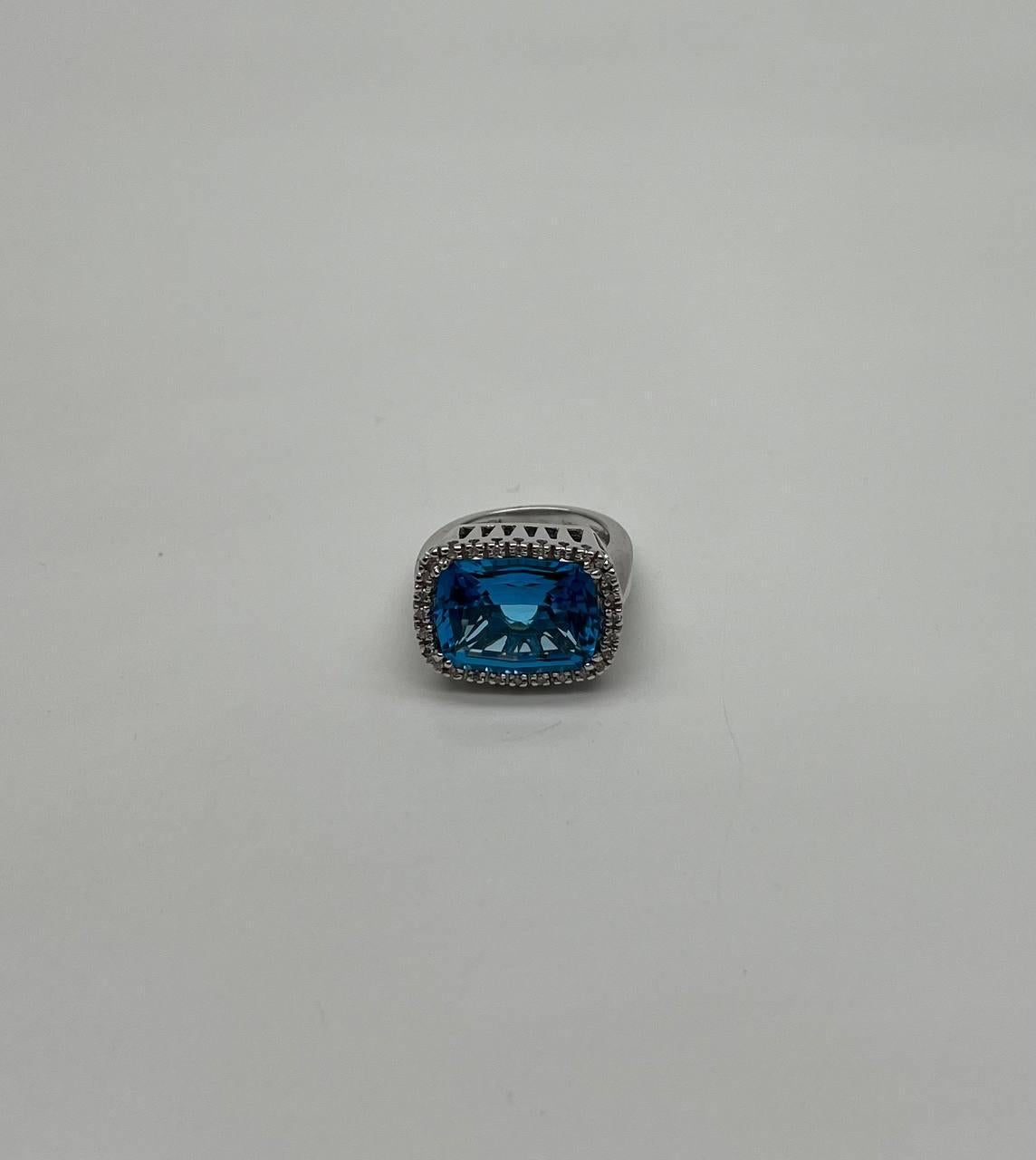 This stunning ring is crafted with precision, featuring a vibrant rectangular blue topaz as the centerpiece. The topaz is surrounded by a delicate halo of sparkling diamonds, enhancing its brilliance. The band is sleek and polished, providing a